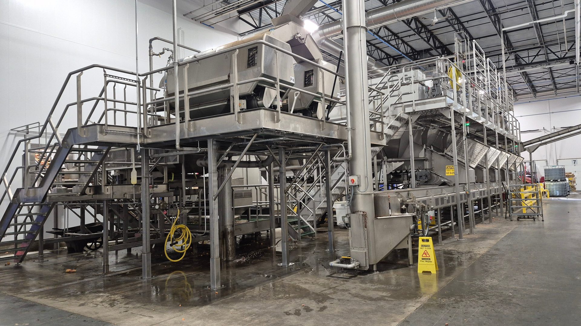 Complex, multi-level stainless steel food processing equipment with platforms and stairs in a factory.