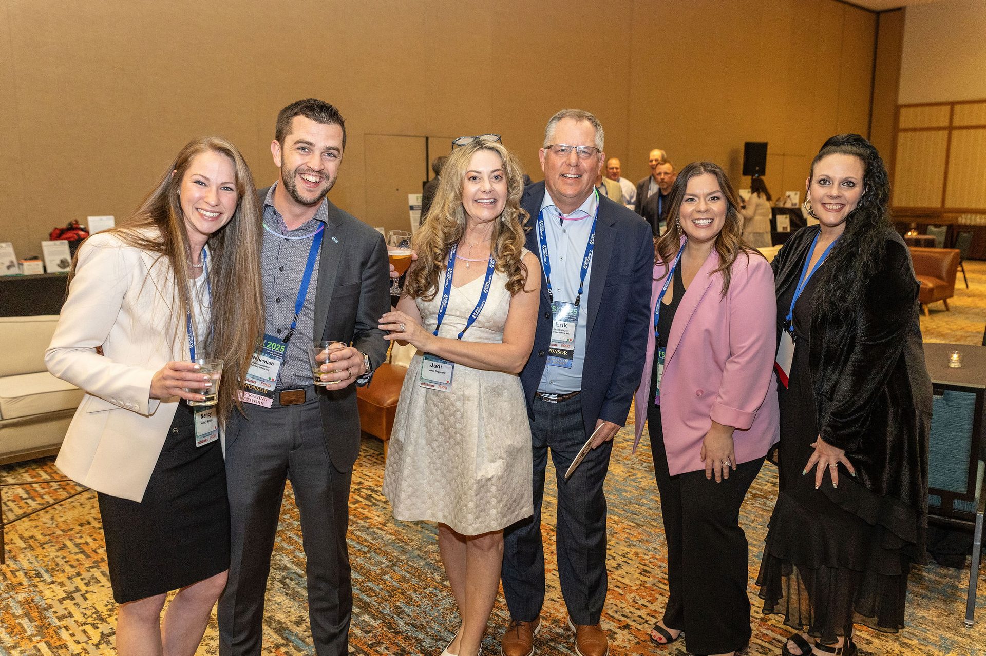 Six smiling people at an event, holding drinks.