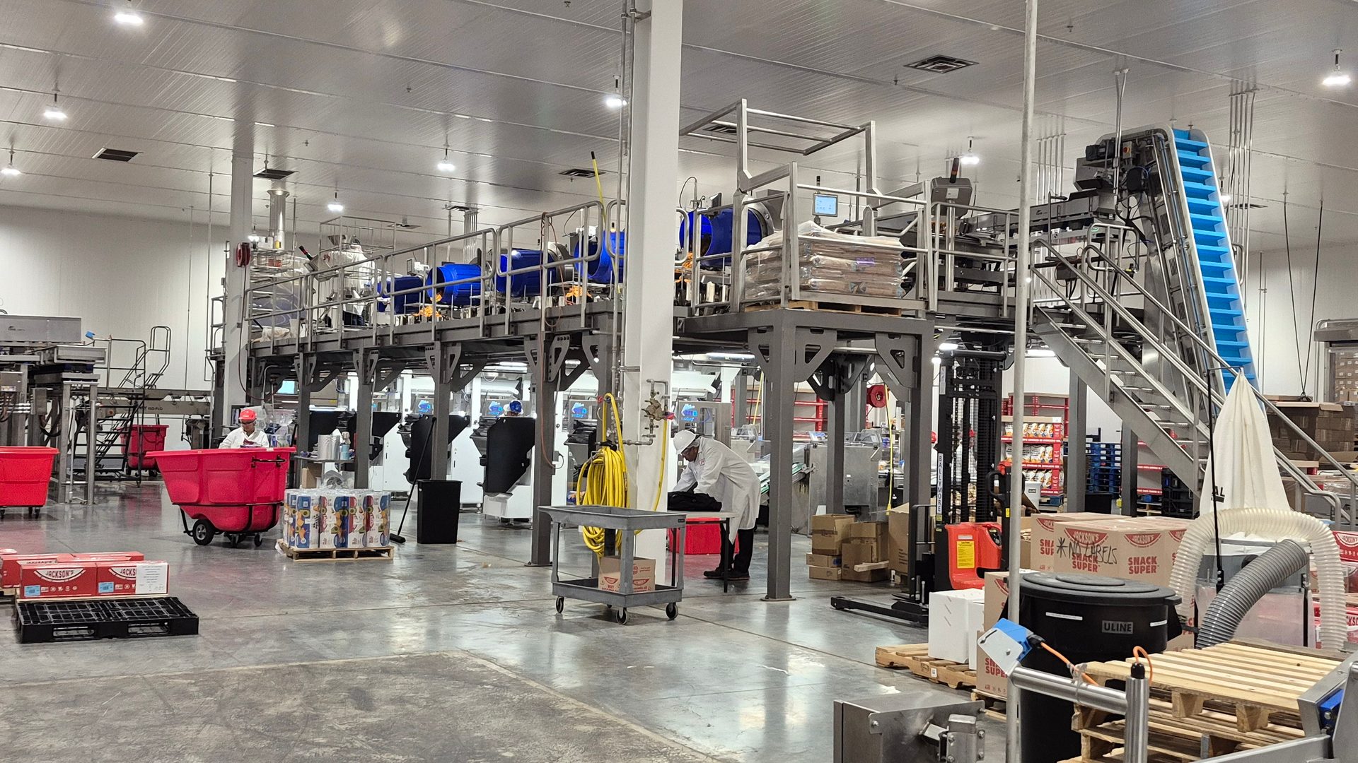 A large-scale food processing facility with complex machinery, conveyors, and workers in protective gear.