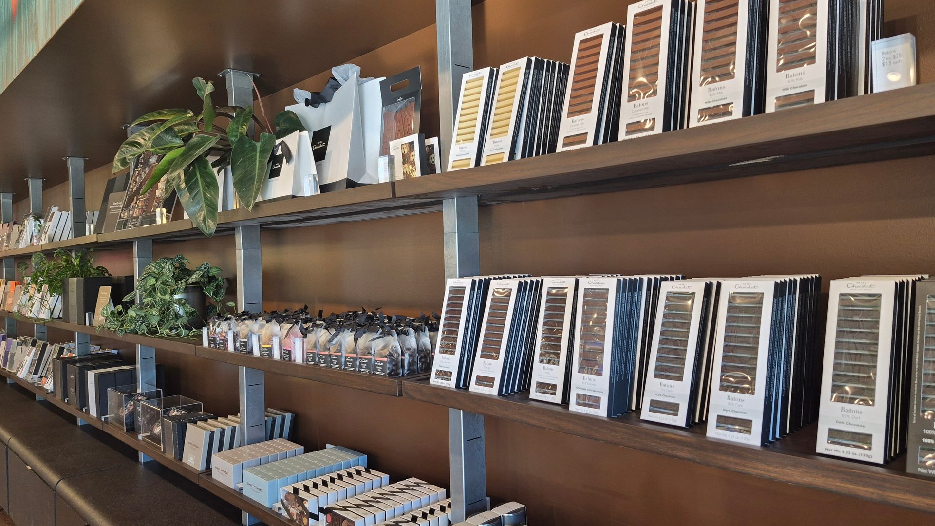 Shelves of Hotel Chocolat products, including various "Batons" chocolate bars and small plants, in a store.