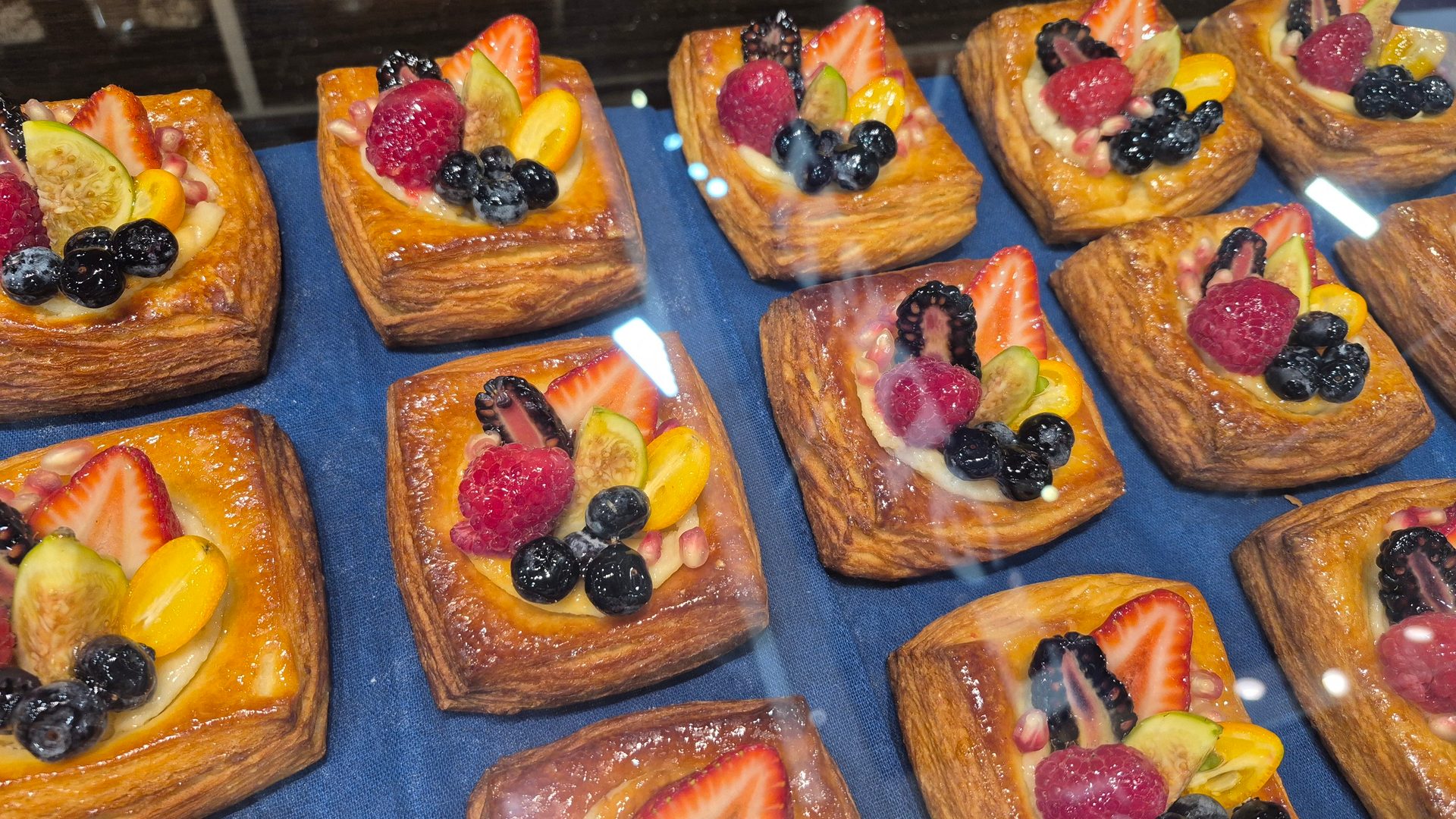 Glazed fruit pastries topped with berries, figs, and kumquats on a blue surface.