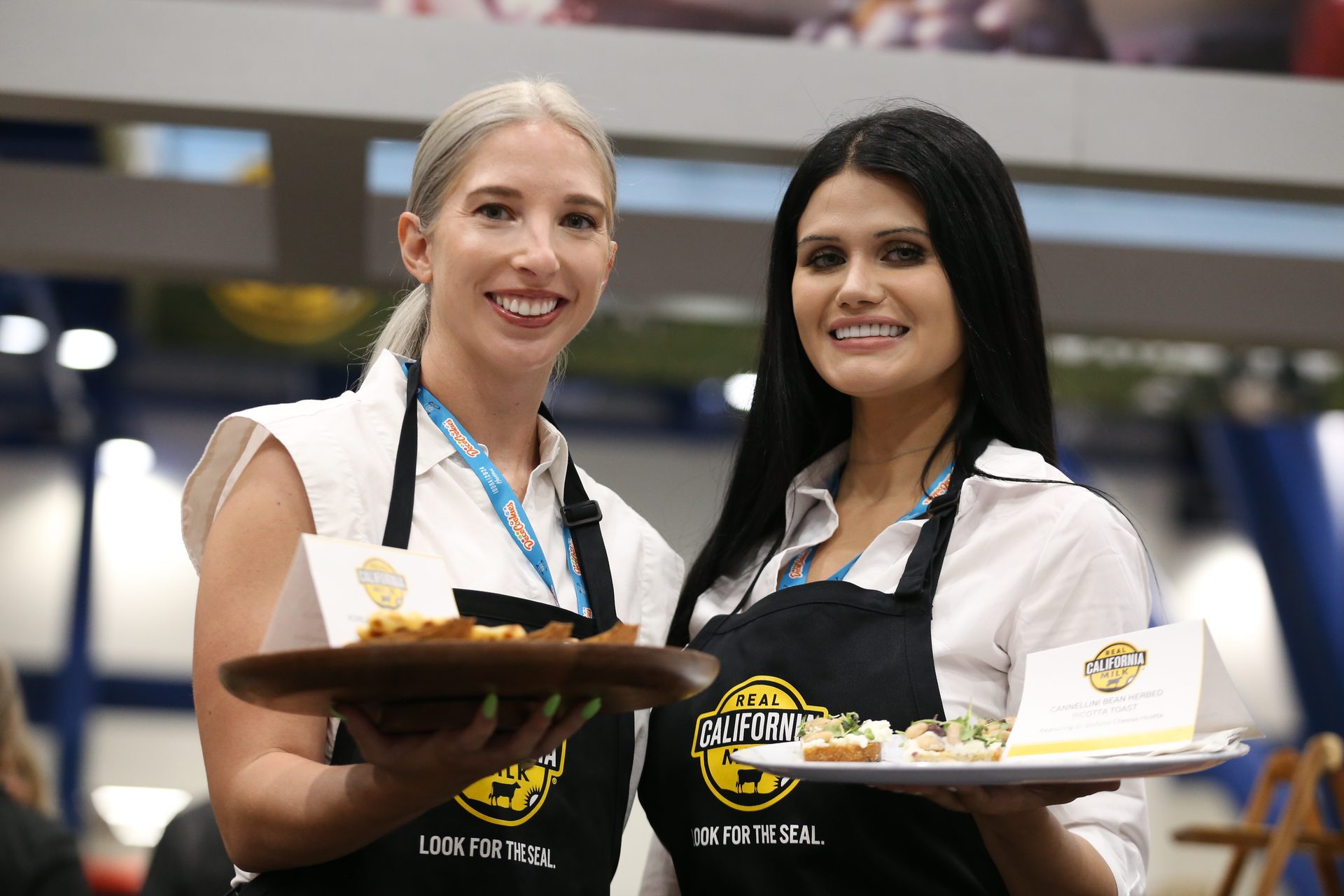 Two women offer samples of bread and cheese on a tray