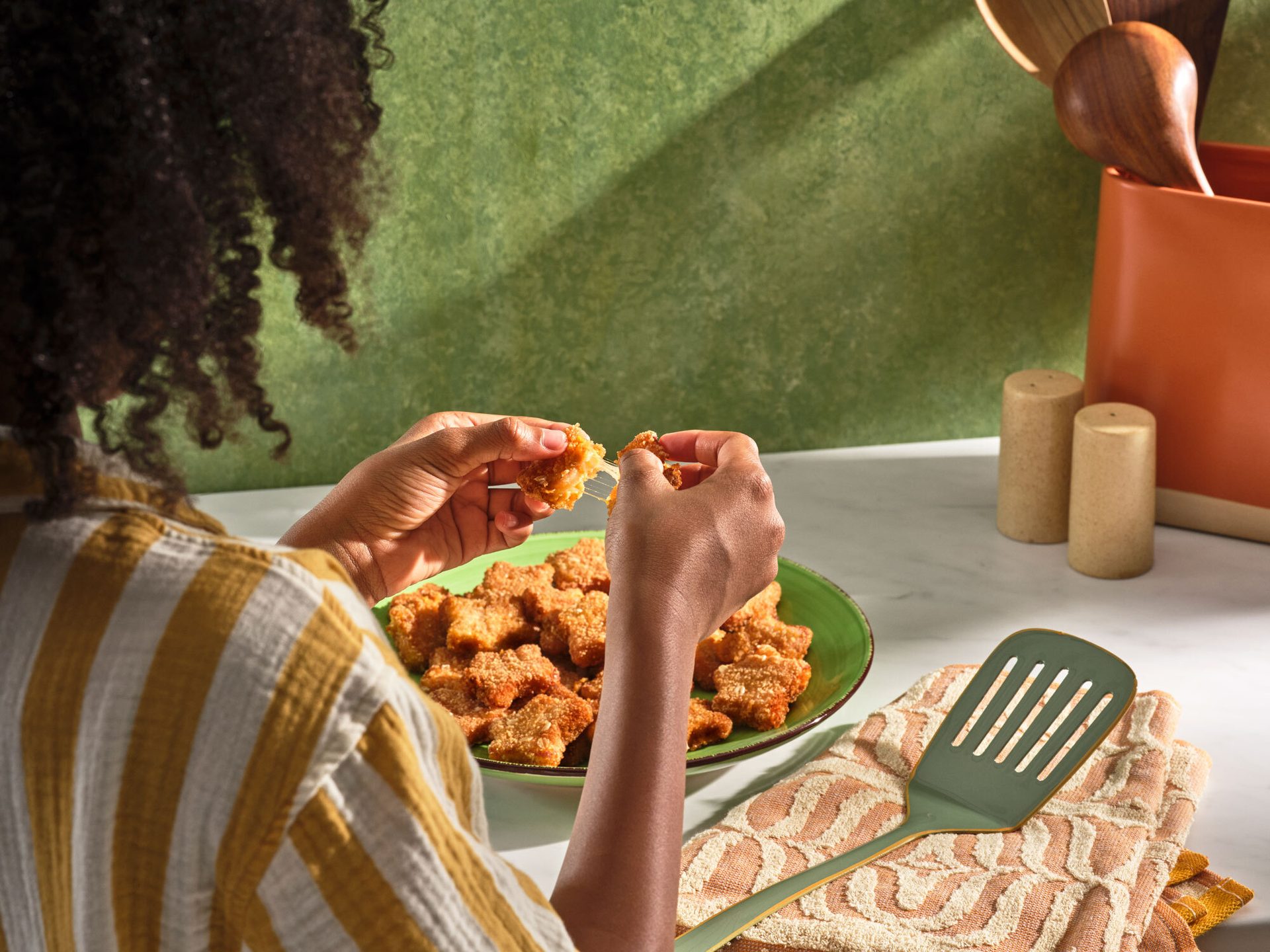 A person pulls apart a crispy fried cheese bite, revealing melted cheese. A plate of bites sits nearby.