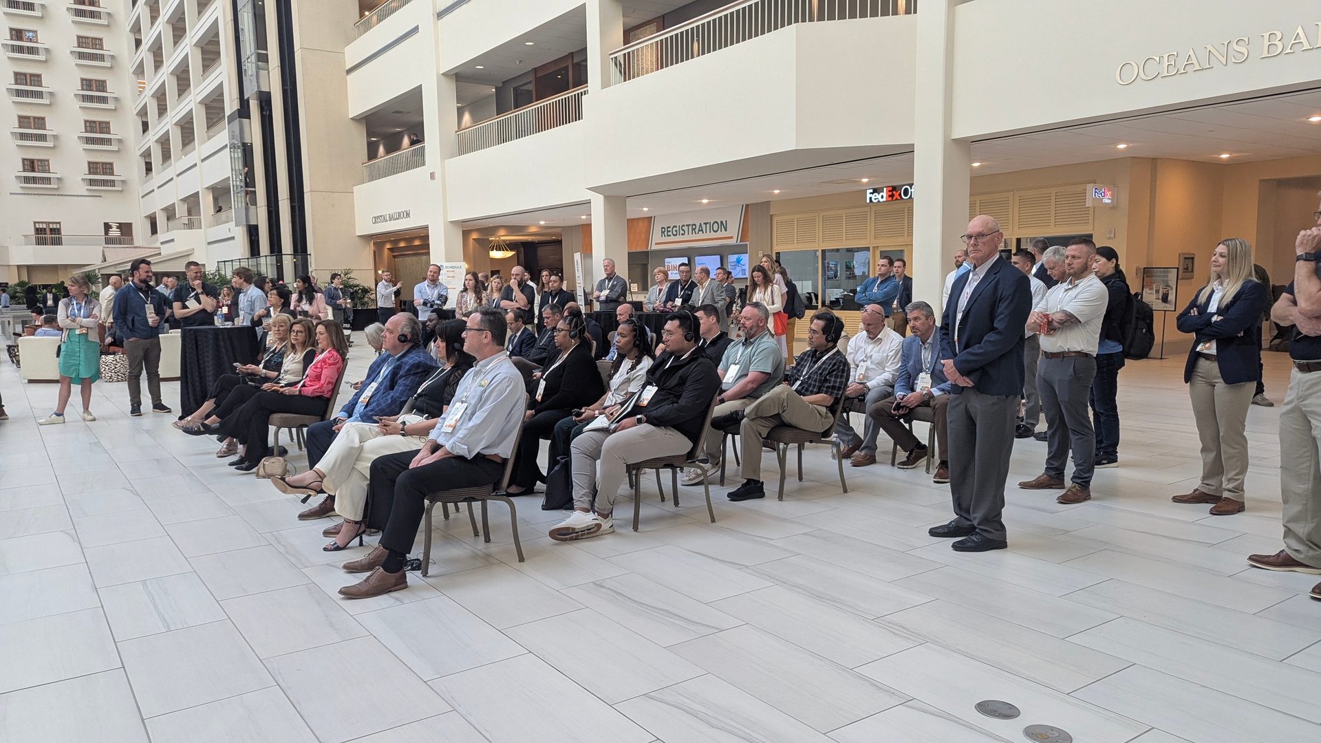 People at an event in a hotel atrium, some seated, some standing.