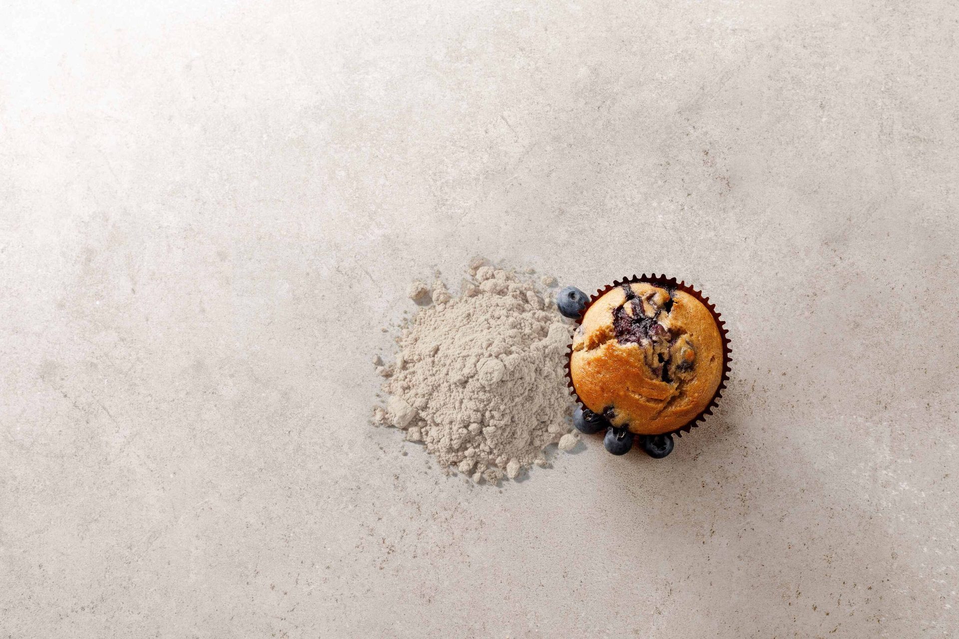 Blueberry muffin, powder, and blueberries on a light textured background.