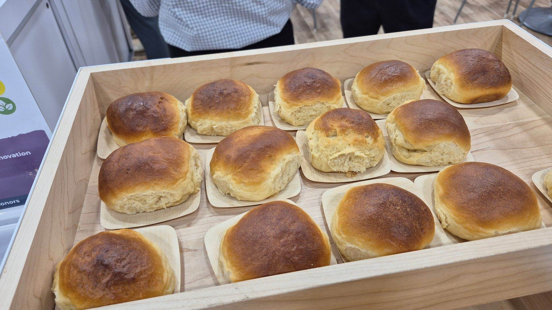 Many golden brown bread rolls on small square plates in a wooden tray.