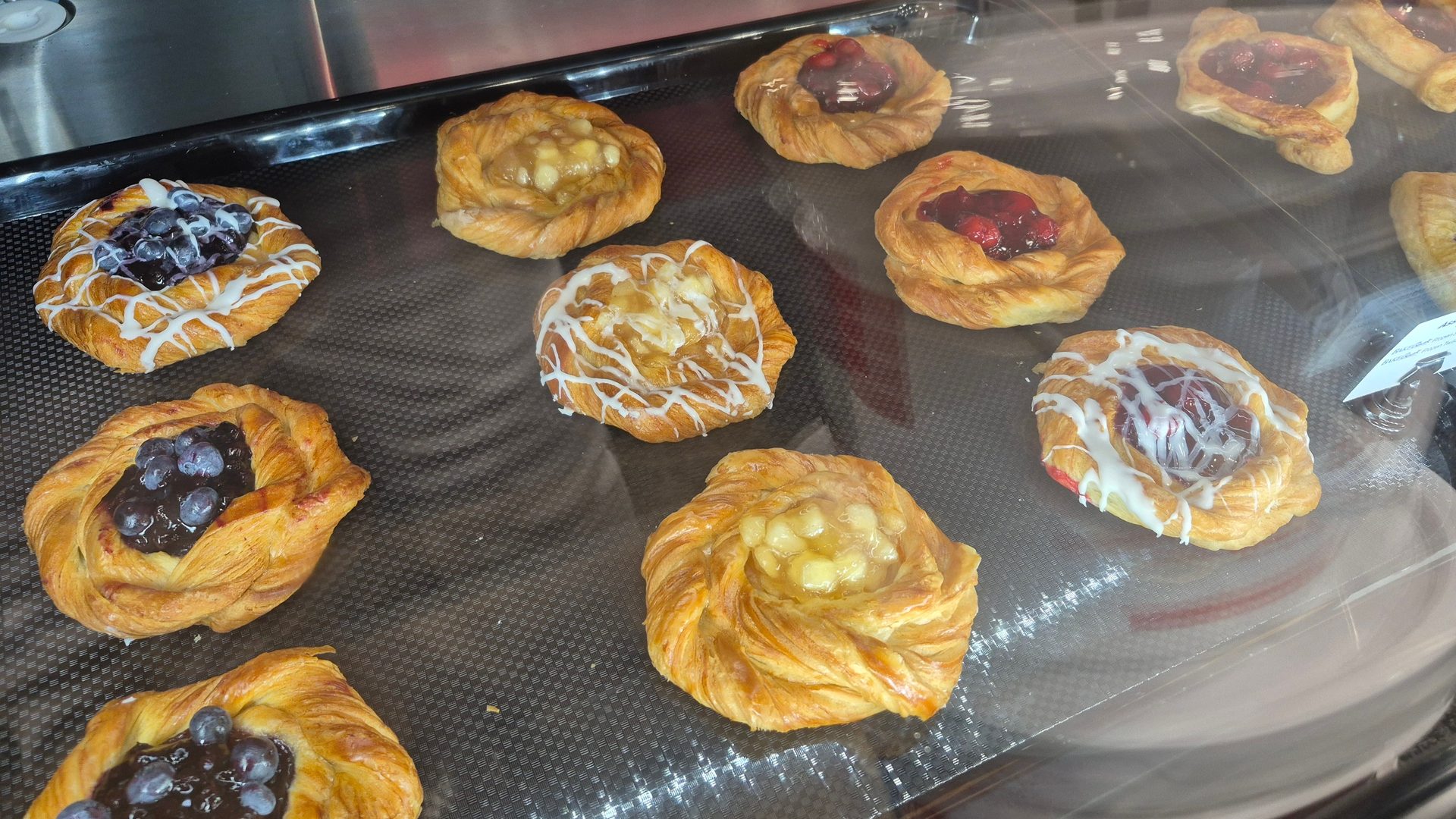 Blueberry, cherry, and apple danishes, some iced, on a dark tray.