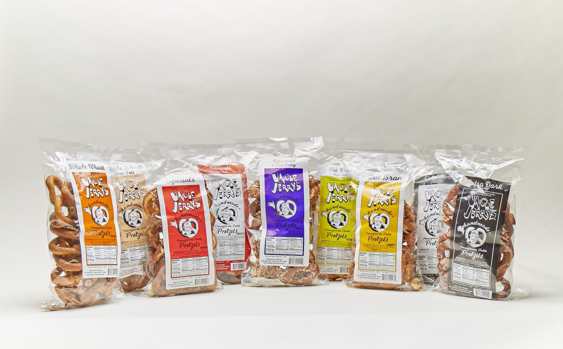 A variety of Uncle Jerry's handmade pretzels in clear bags with colorful labels, lined up on a white surface.
