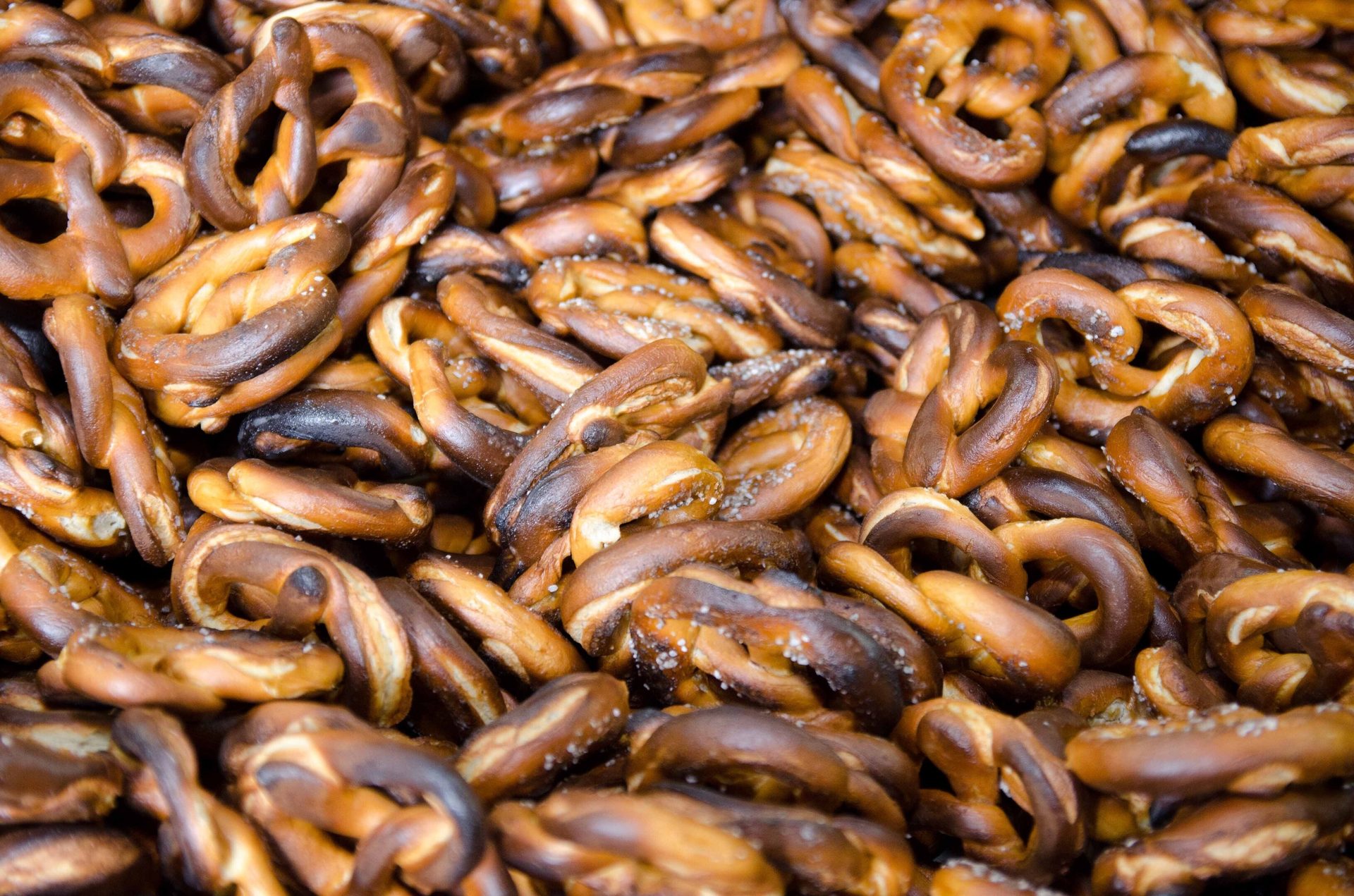 A large pile of golden-brown and dark pretzels, many sprinkled with salt, filling the frame.