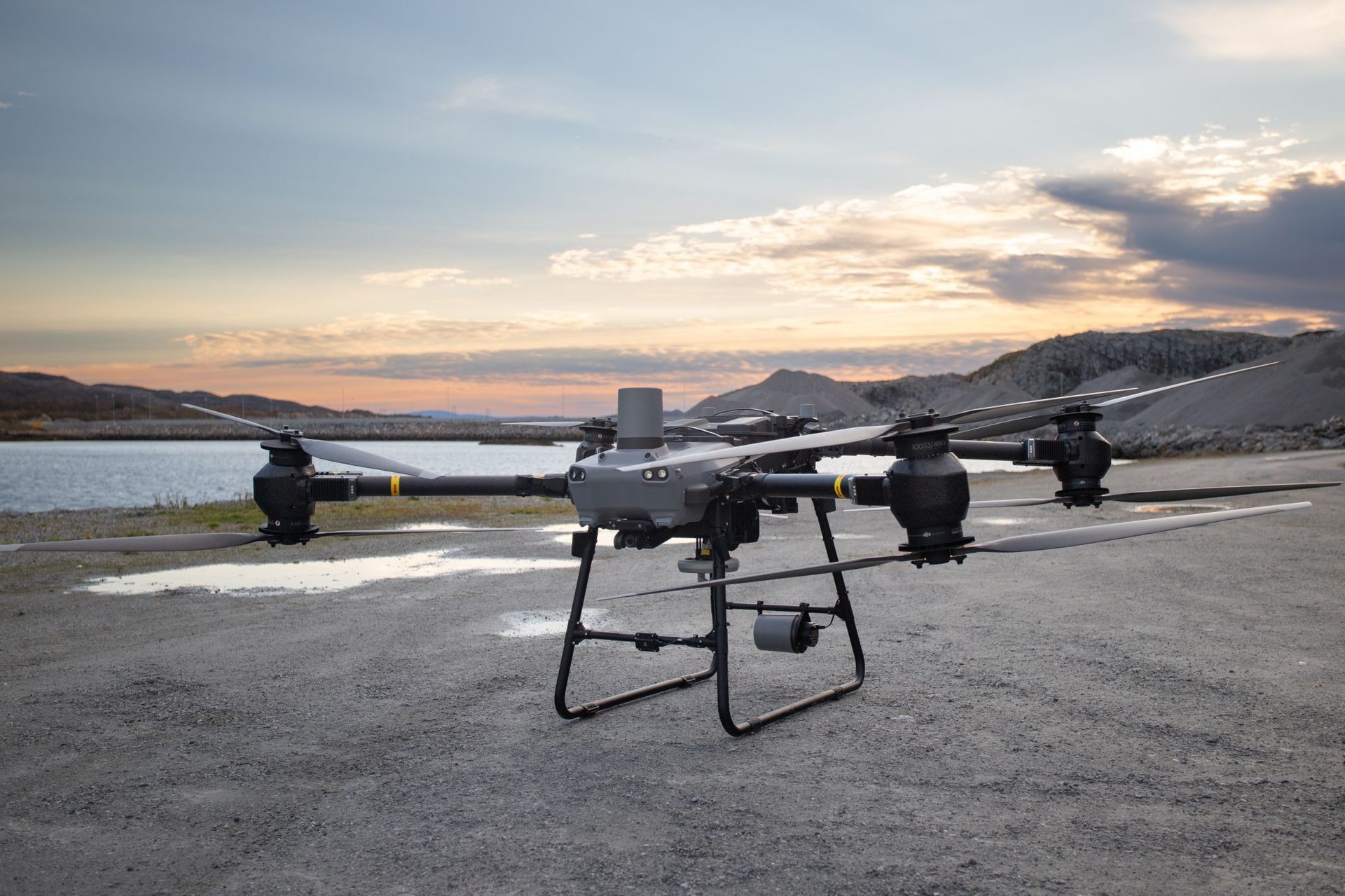 Grey octocopter drone on the ground, sunset over water and mountains.