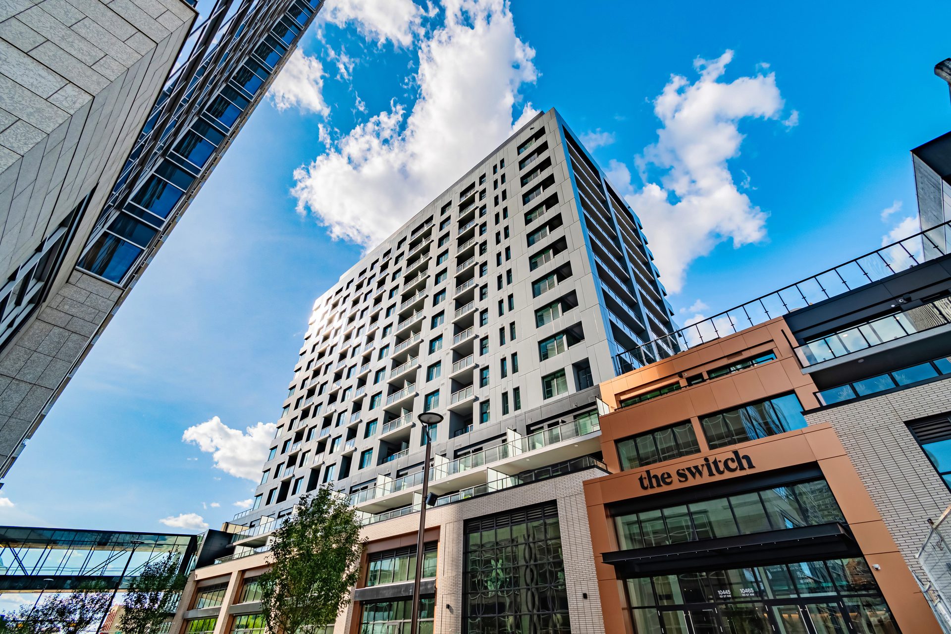 Modern high-rise buildings, one with "the switch" sign, against a blue sky with clouds.