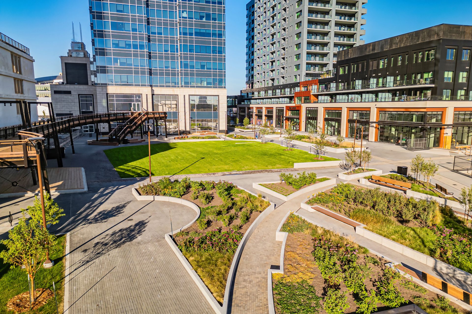 Aerial view of a modern urban plaza with tall buildings, a green lawn, and landscaped walkways.