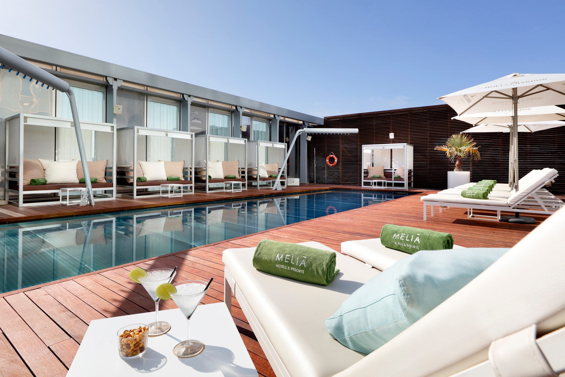 Luxury rooftop pool with modern cabanas, sun loungers, and cocktails in a sunny resort setting.