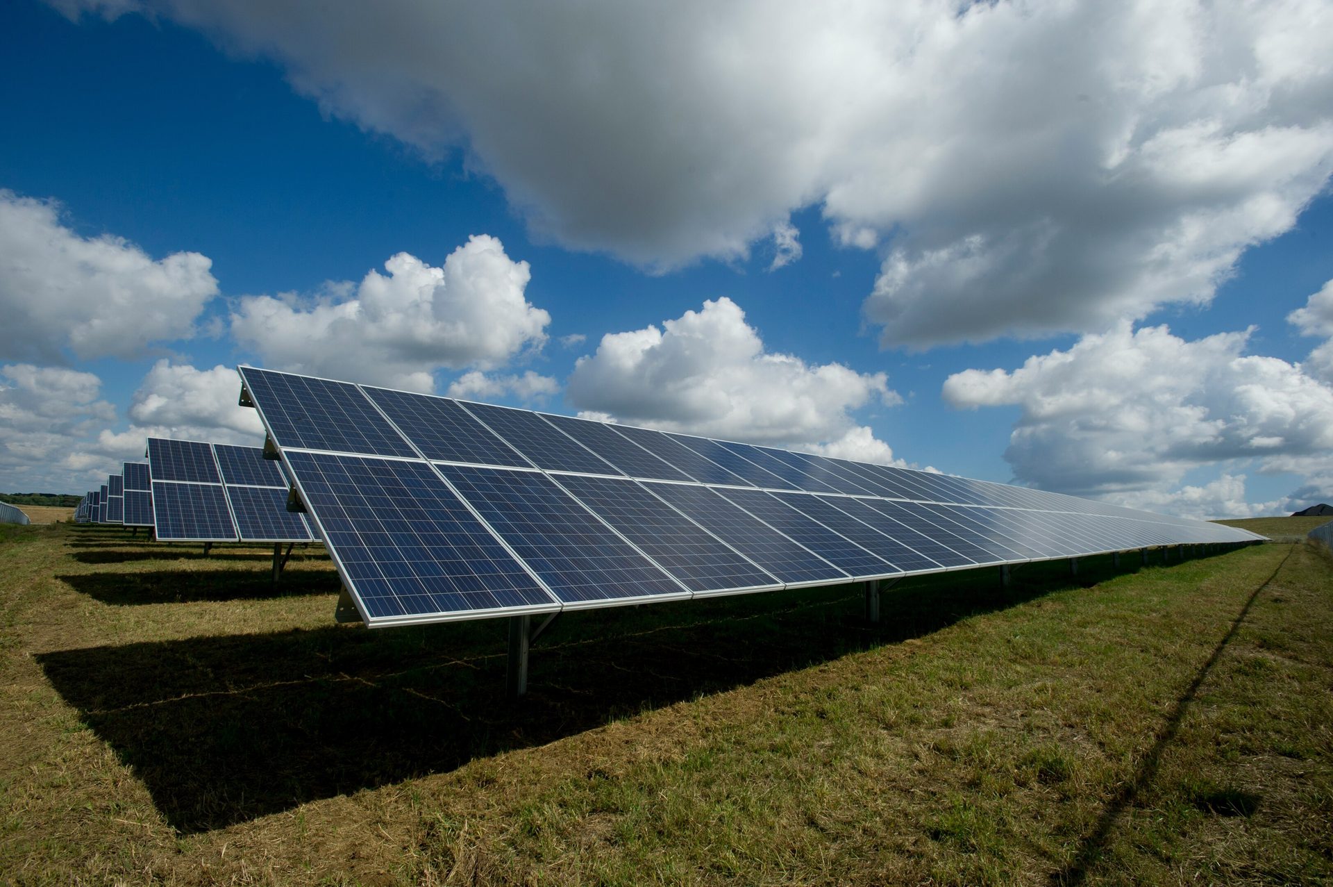 Rows of solar panels in a field under a cloudy sky.