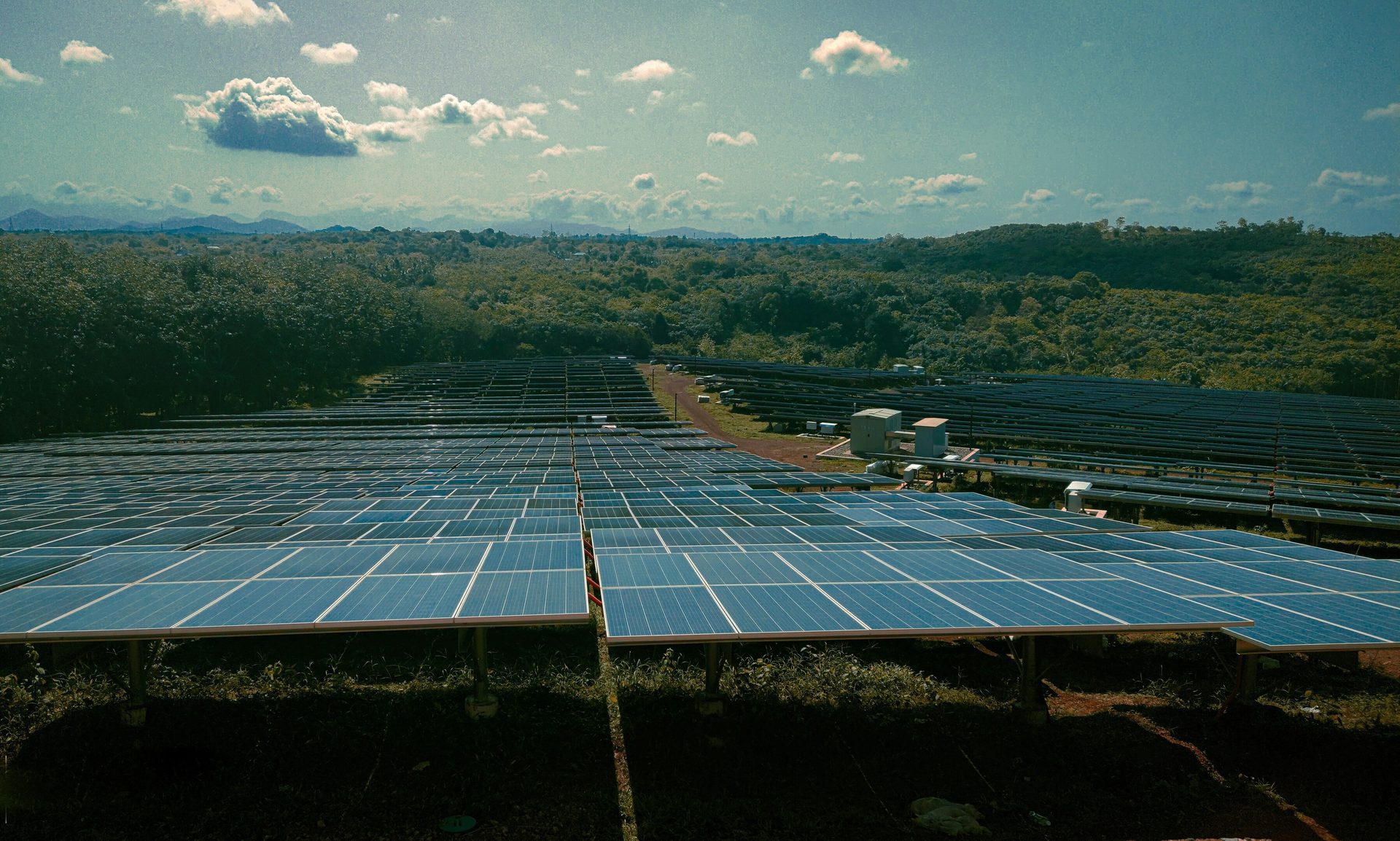 A large solar farm in a green landscape under a cloudy sky.