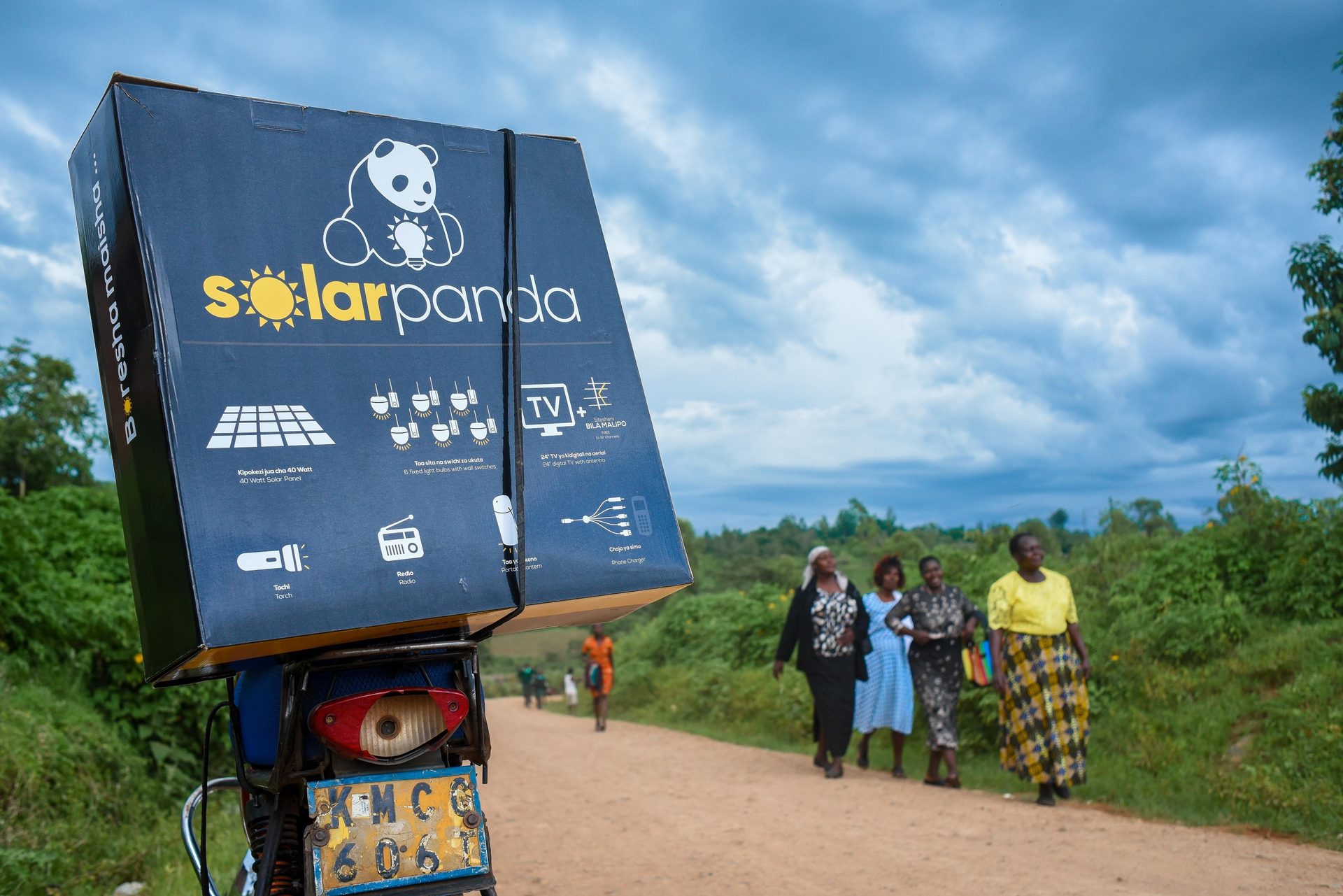Solar Panda box on motorcycle with people walking on a dirt road.