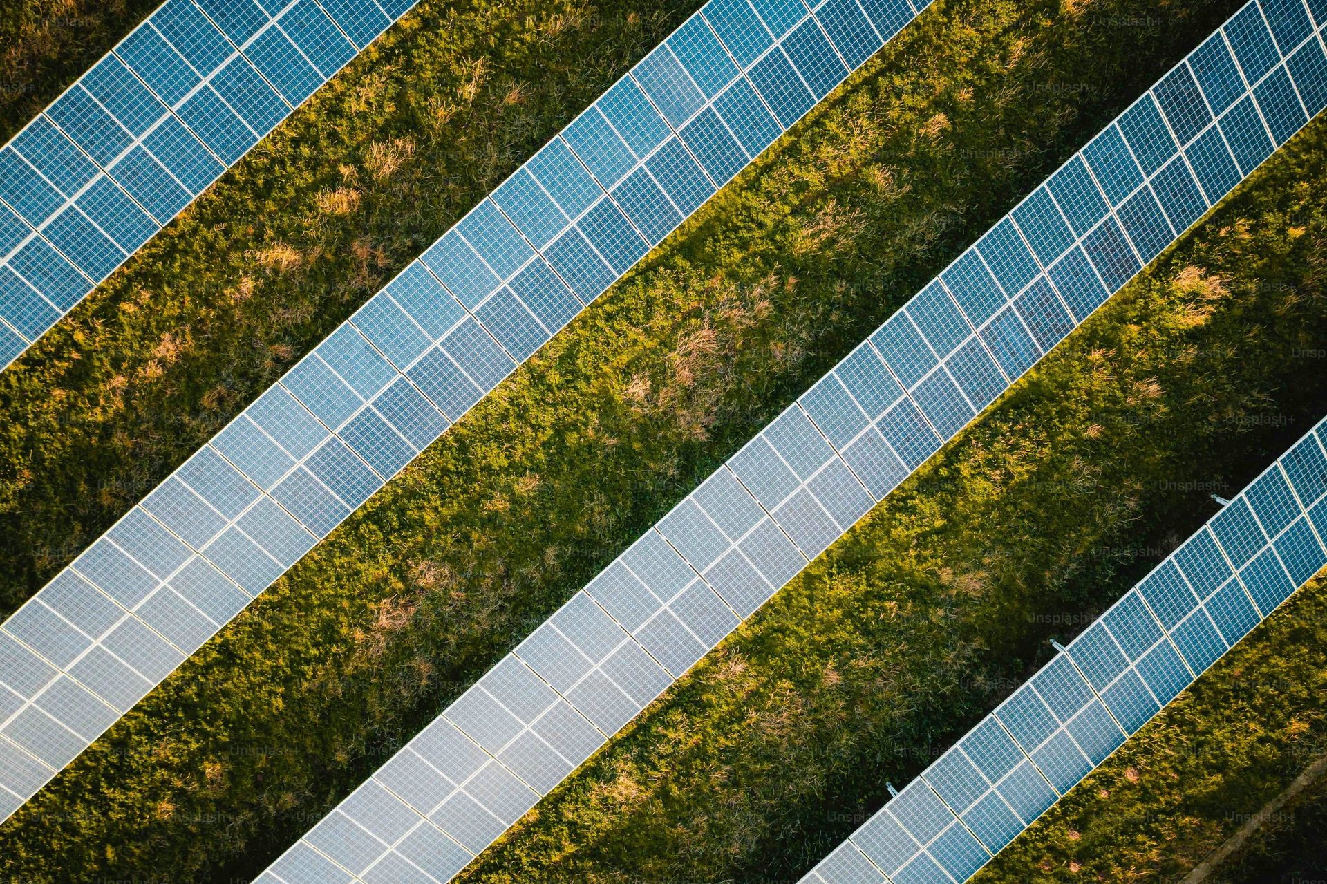 Aerial view of diagonal solar panel rows on grassy terrain.