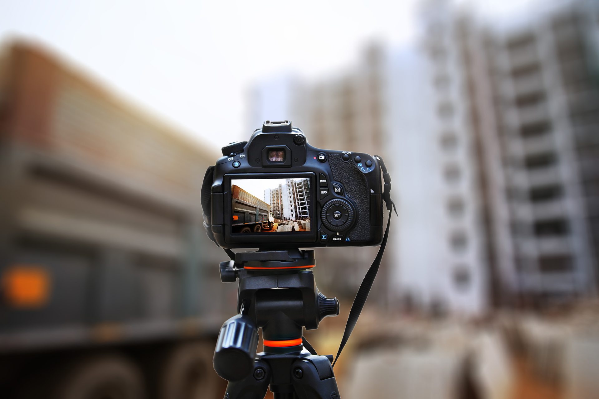 DSLR camera on a tripod, its screen showing a construction site, against a blurred construction background.