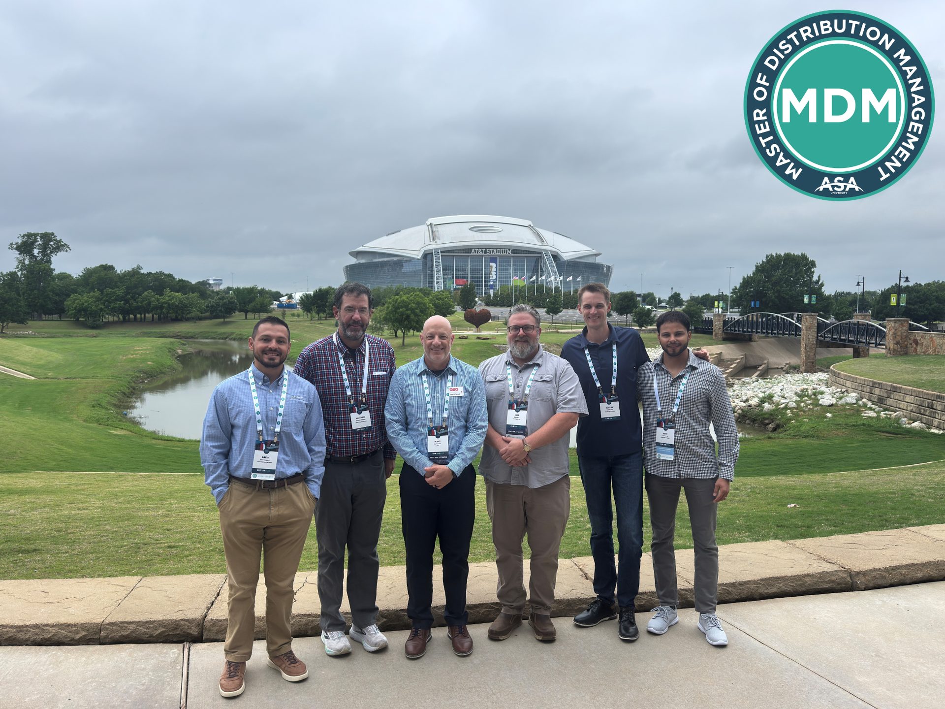 Six men from the MDM program pose for a group photo outside AT&T Stadium with a pond.