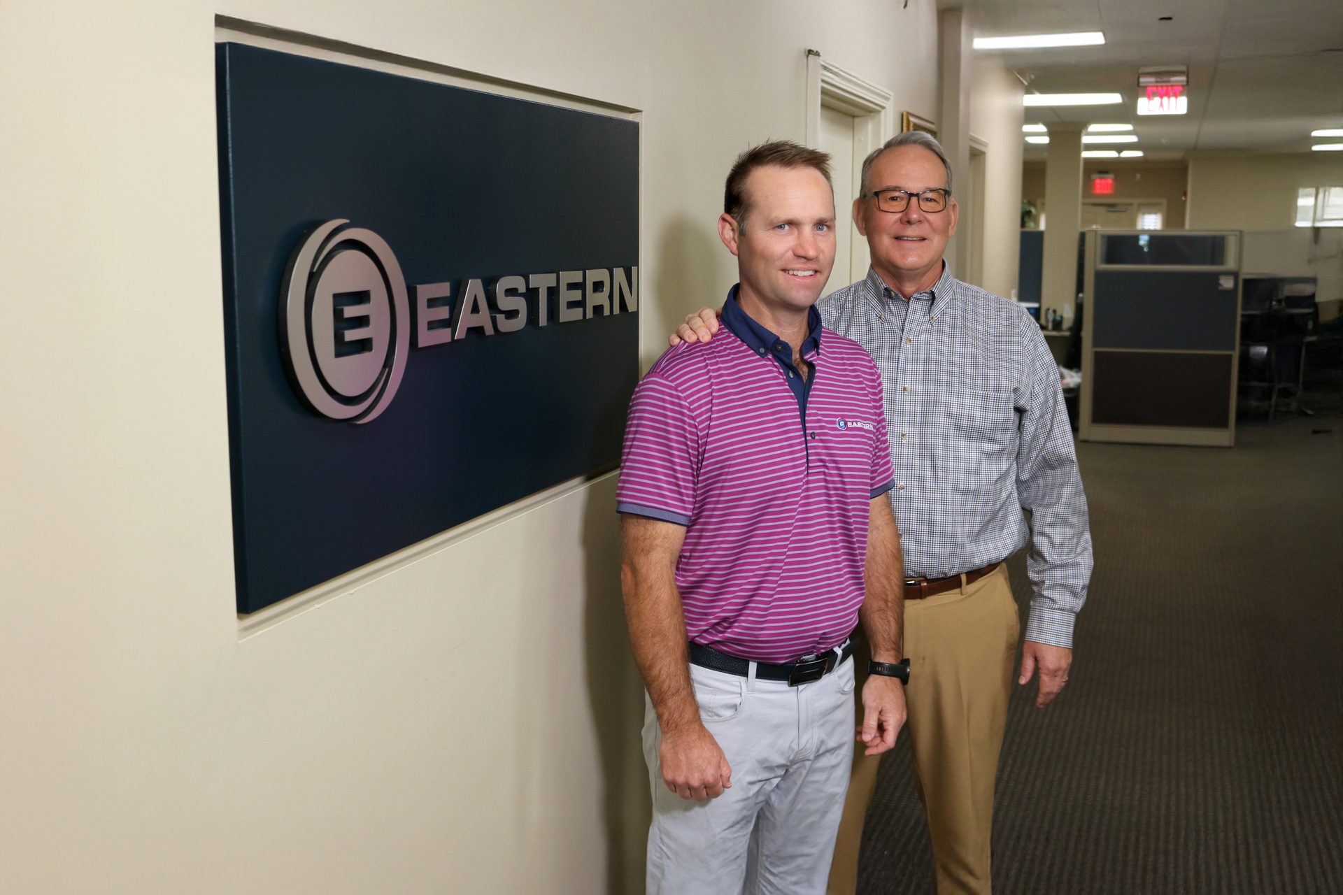 Two men stand in an office hallway next to an "EASTERN" company sign.