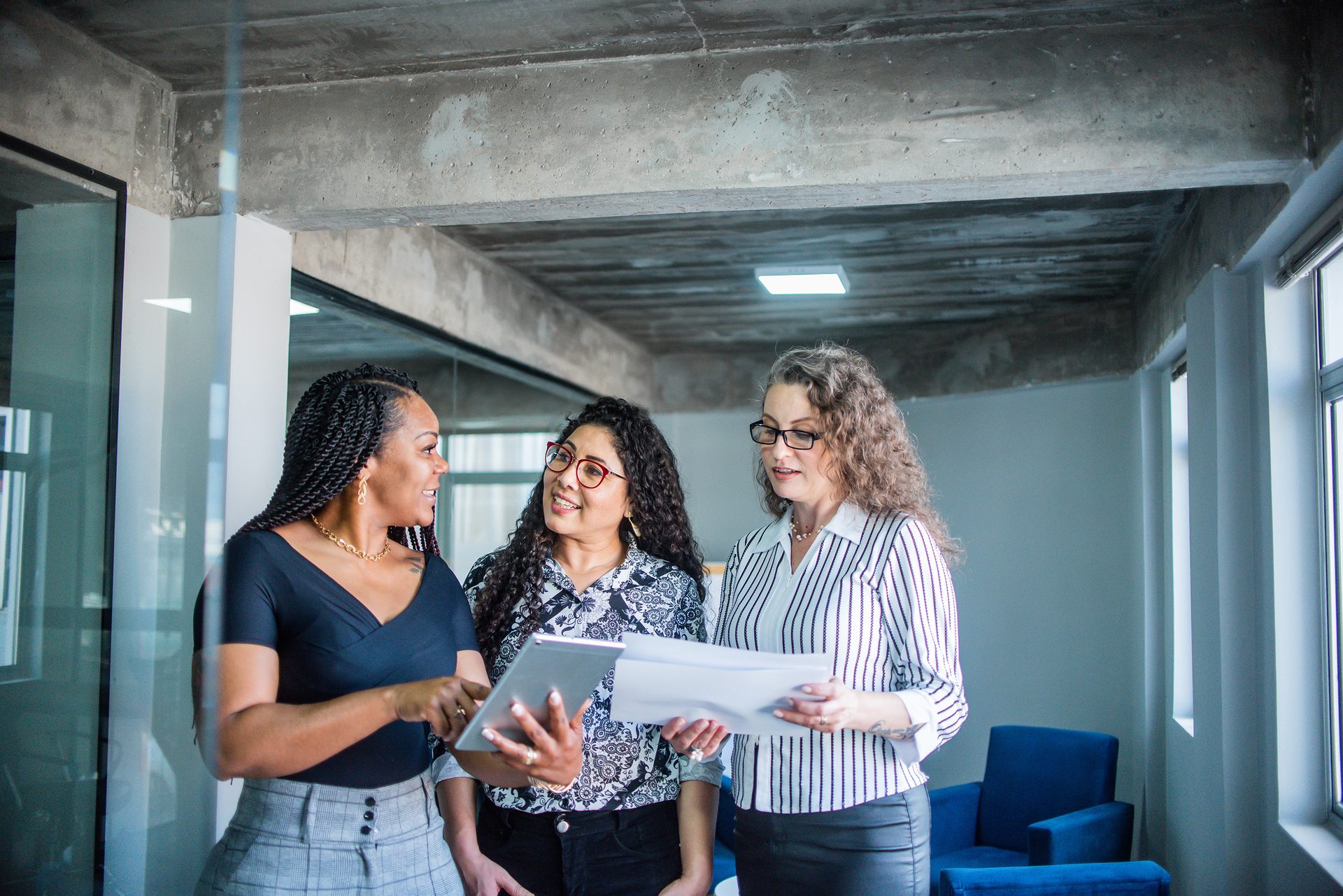 Three women in an office collaborating, using a tablet and papers.
