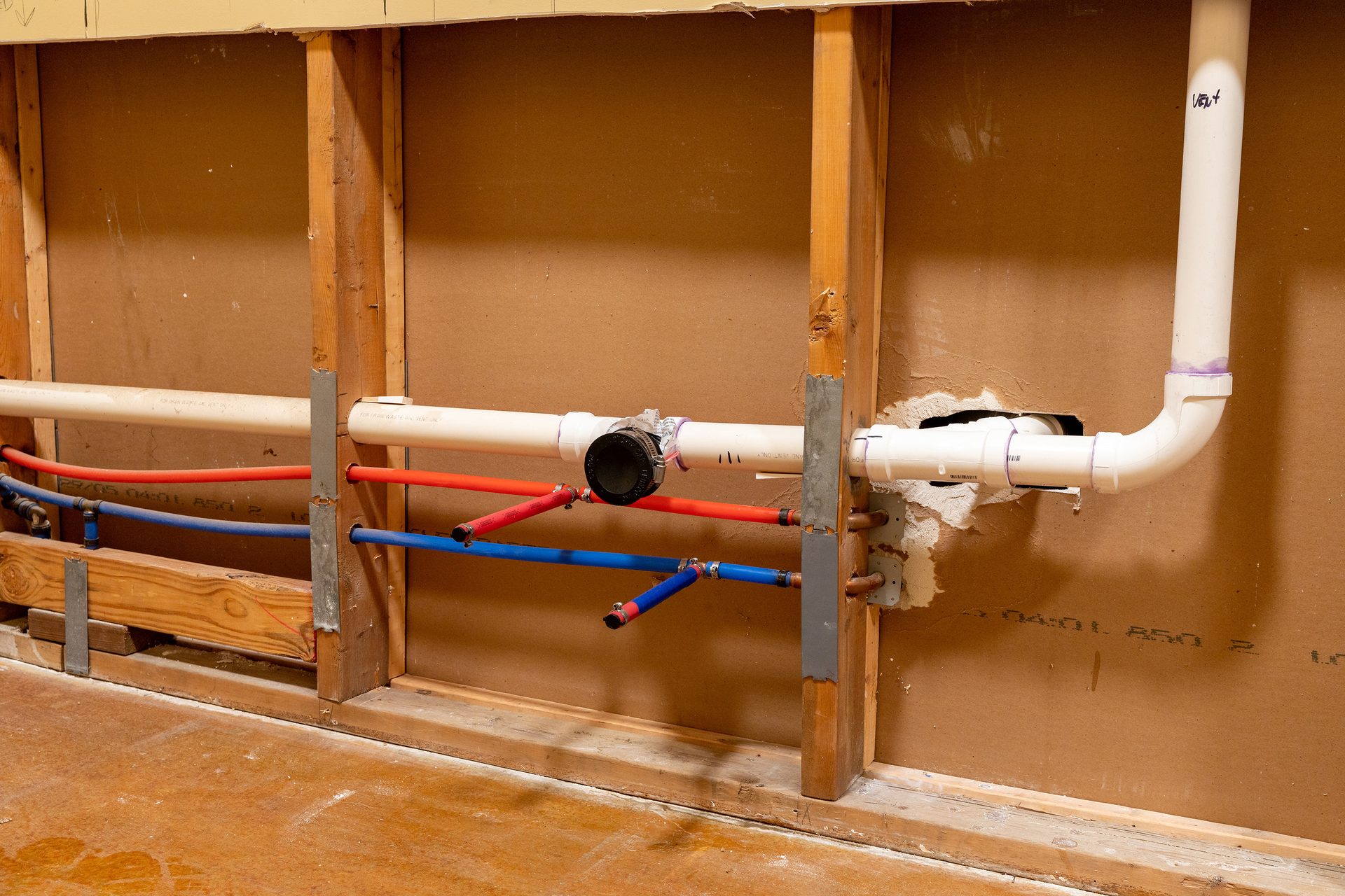 Exposed rough-in plumbing with PVC drain/vent pipes and red/blue PEX water lines in a wall.