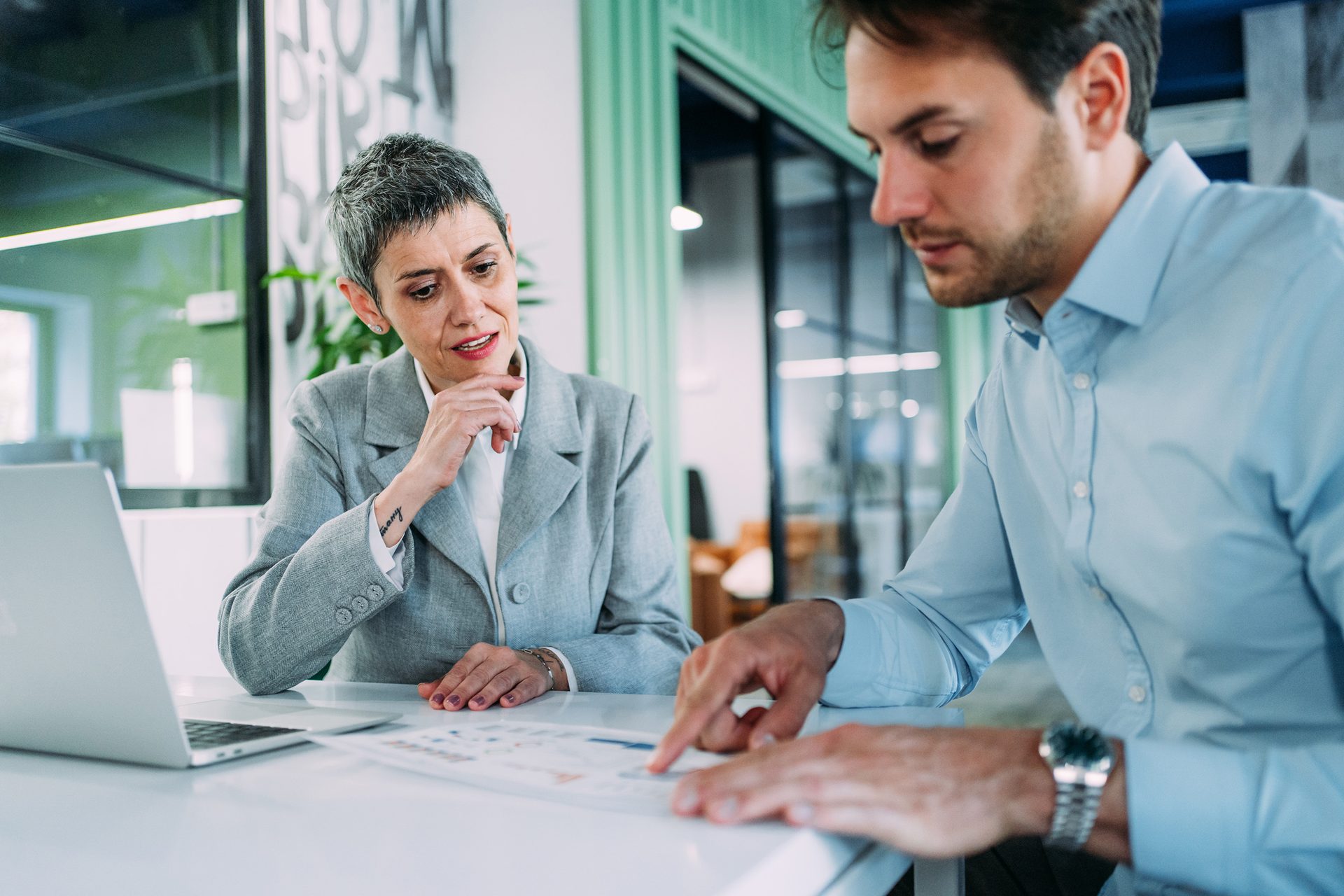 Two business professionals discuss documents during a meeting in a modern office.