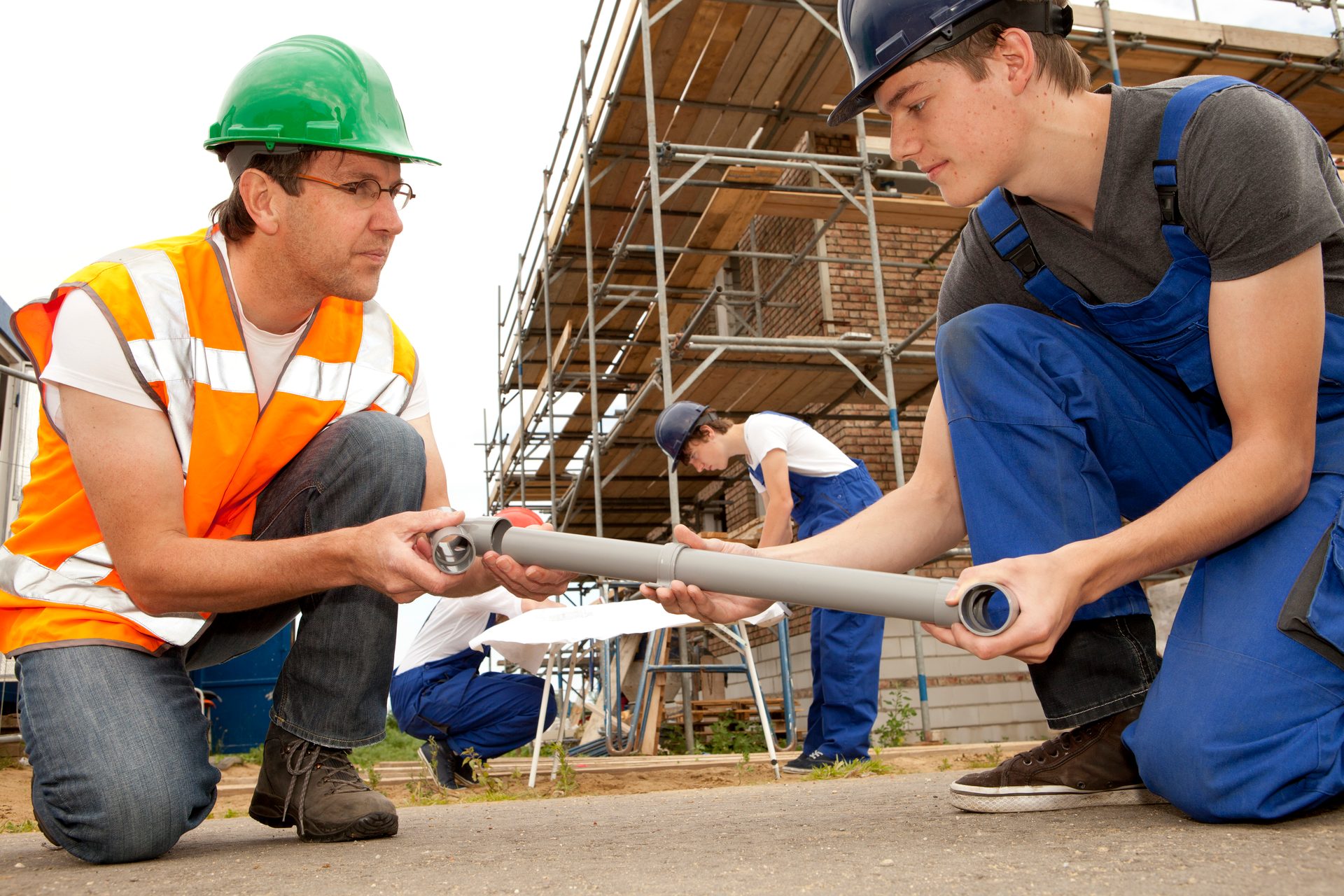Older and younger construction workers fitting pipes on a building site.
