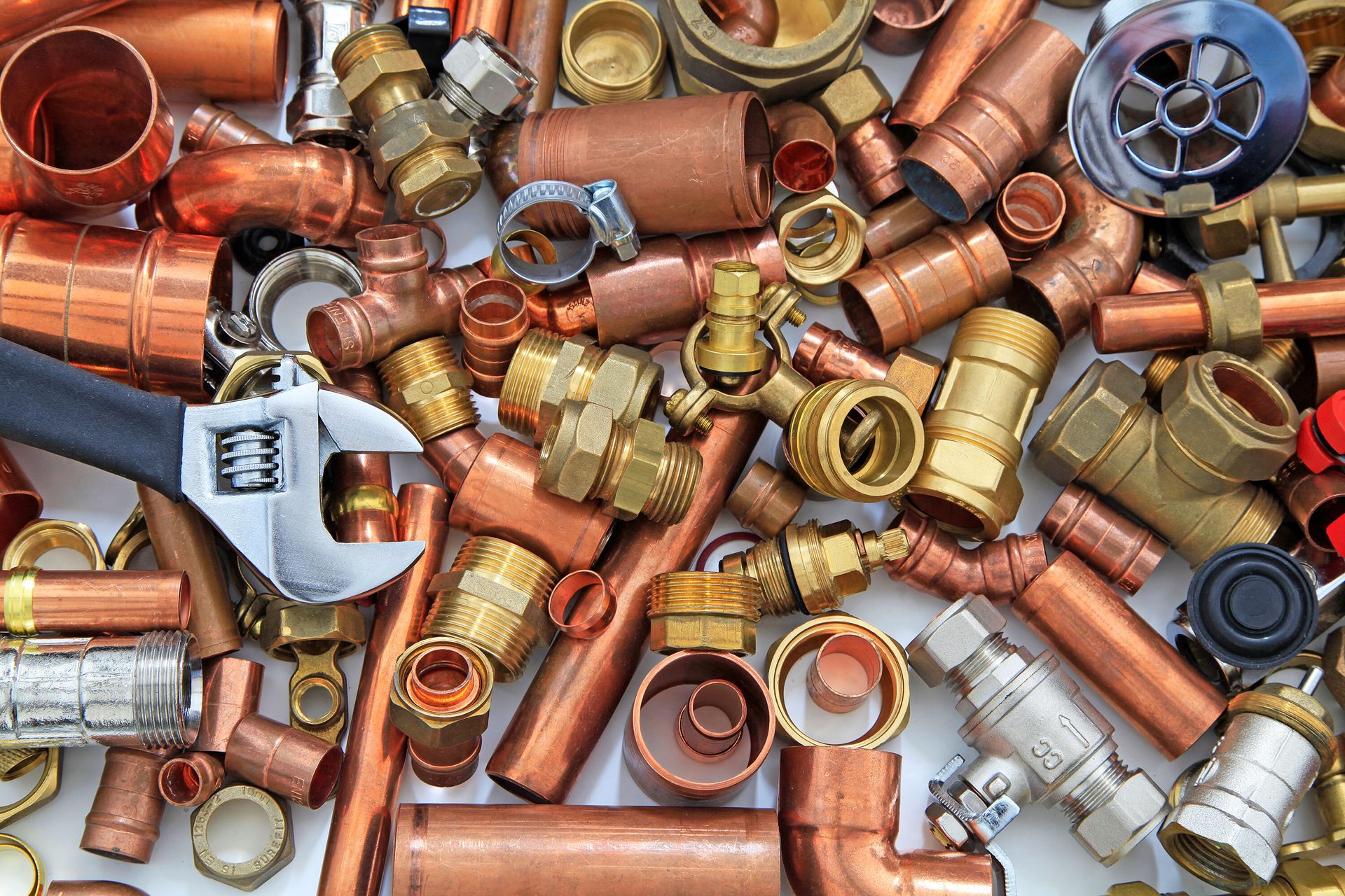 A pile of various plumbing parts, including copper pipes, brass fittings, and an adjustable wrench.