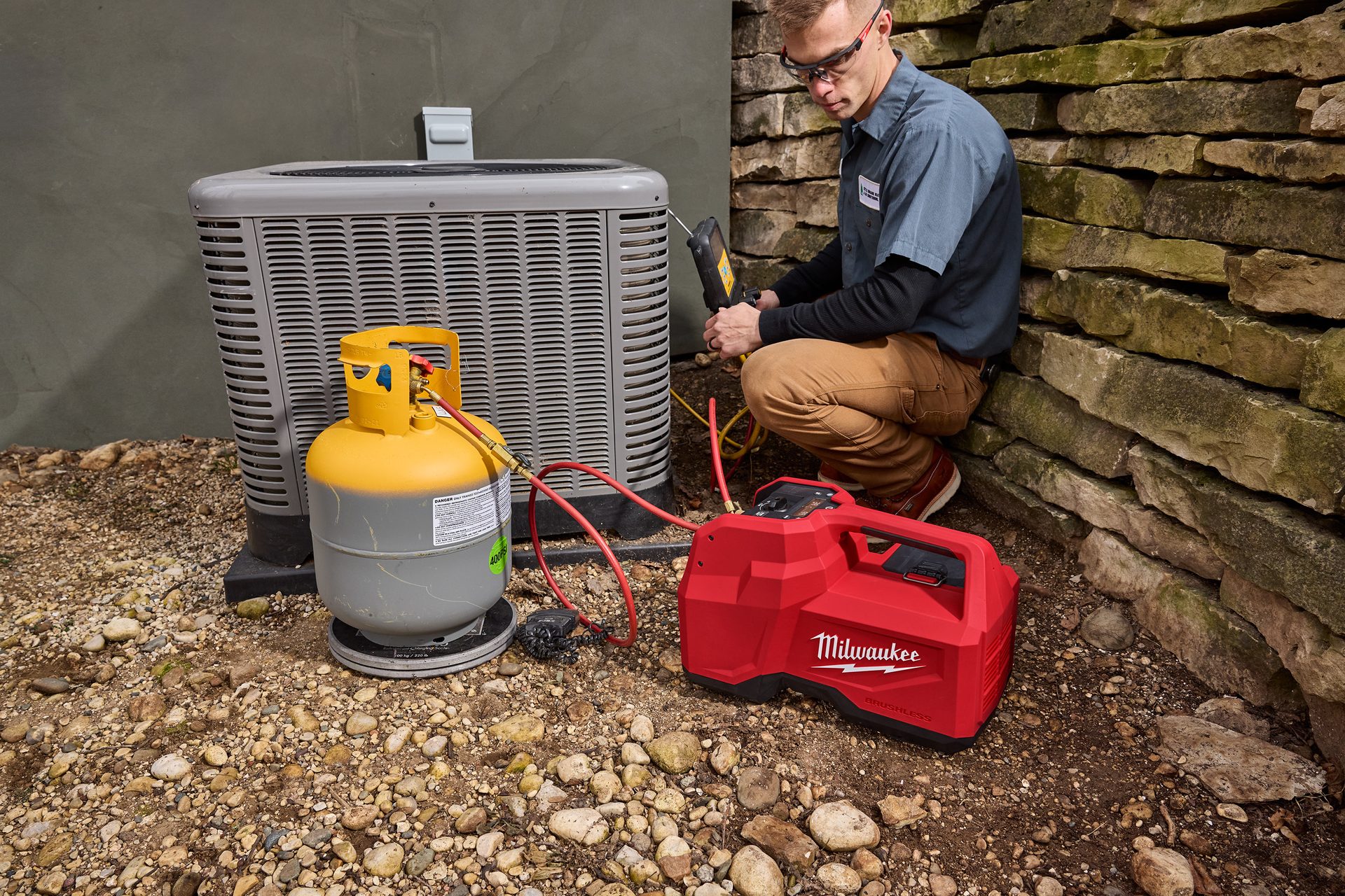 HVAC technician servicing an AC unit with a Milwaukee recovery machine and refrigerant tank.