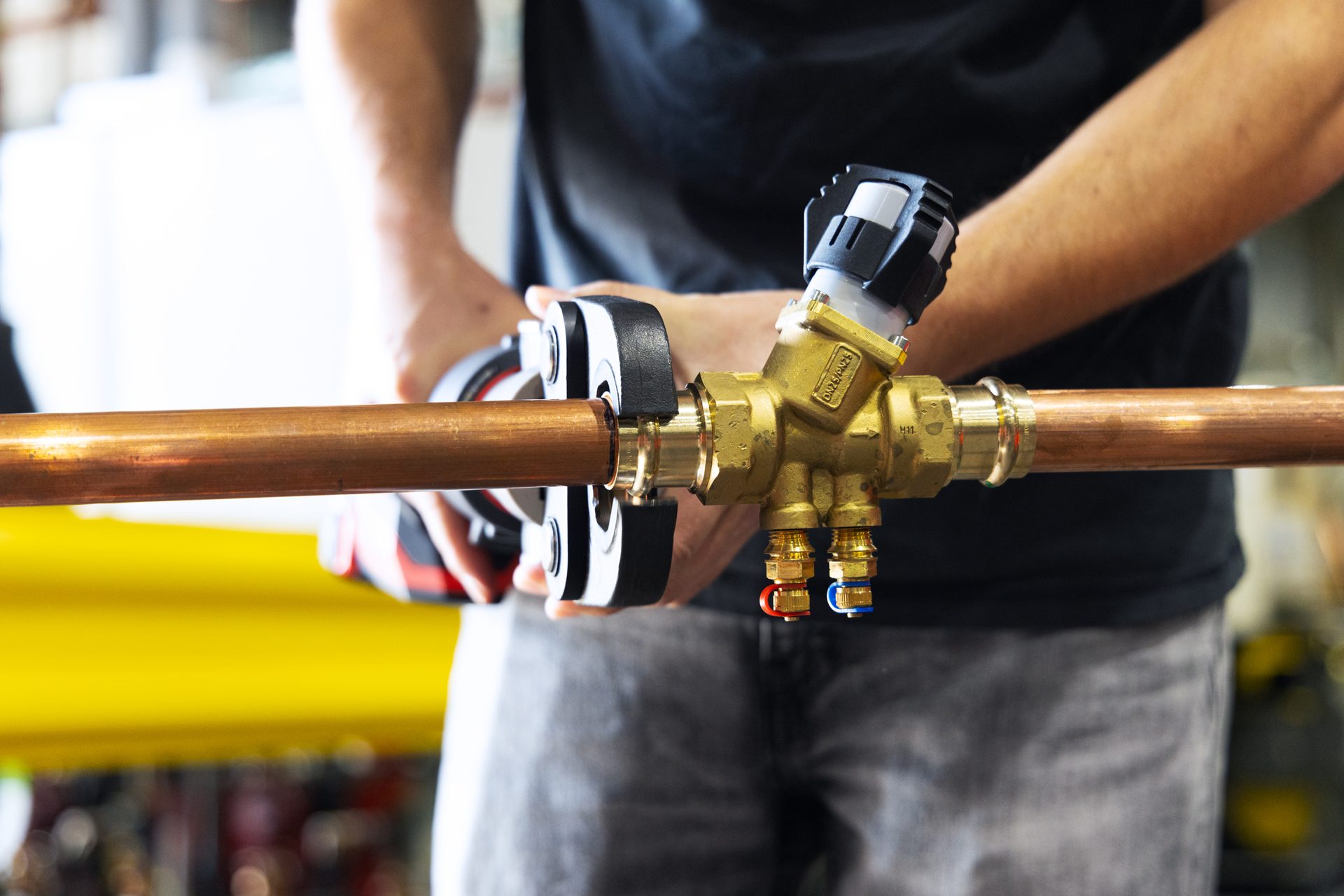 A plumber installs a brass valve onto a copper pipe using a press tool.