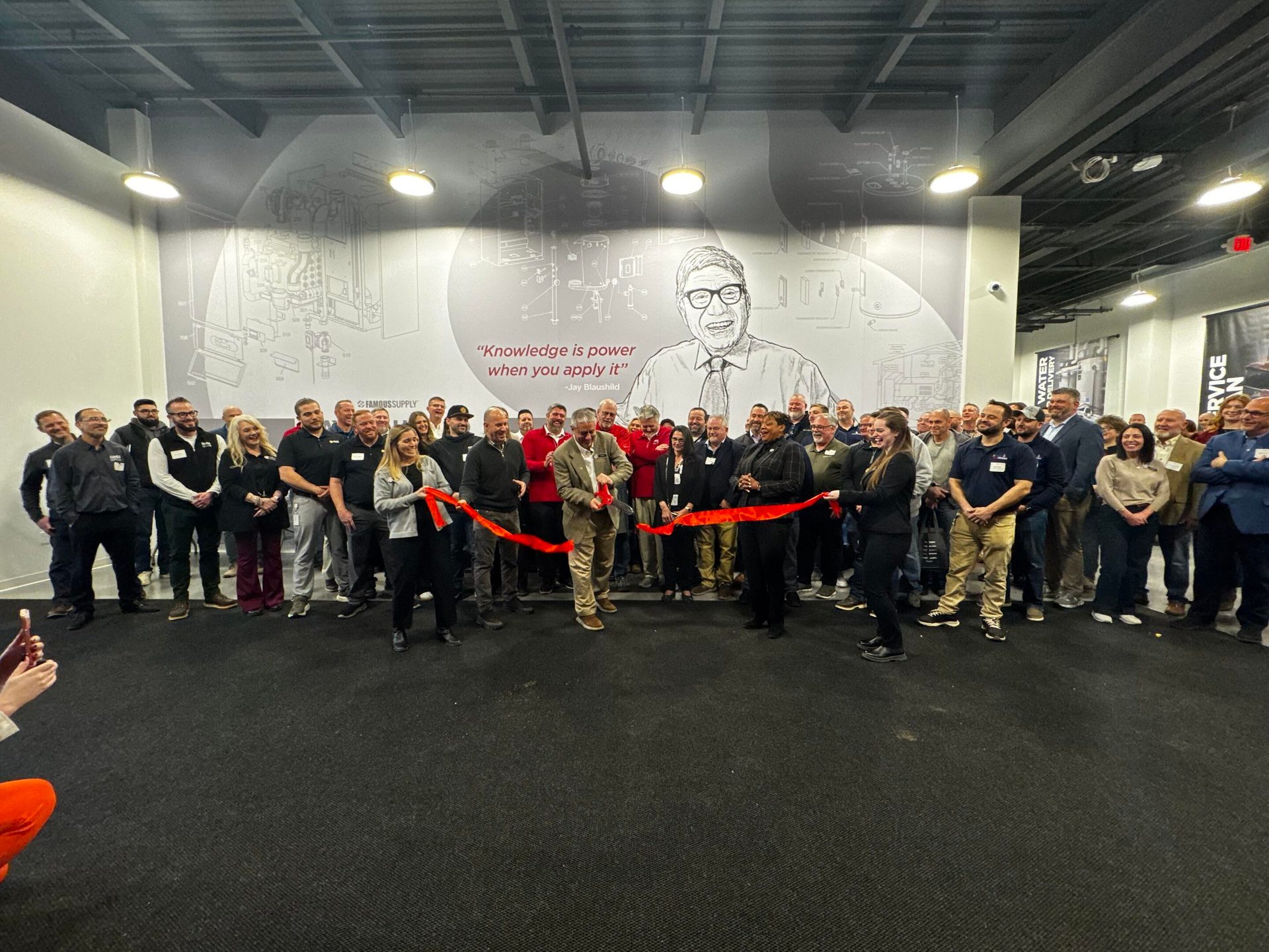A group of people at a ribbon-cutting ceremony, with a "Knowledge is power when you apply it" mural behind.