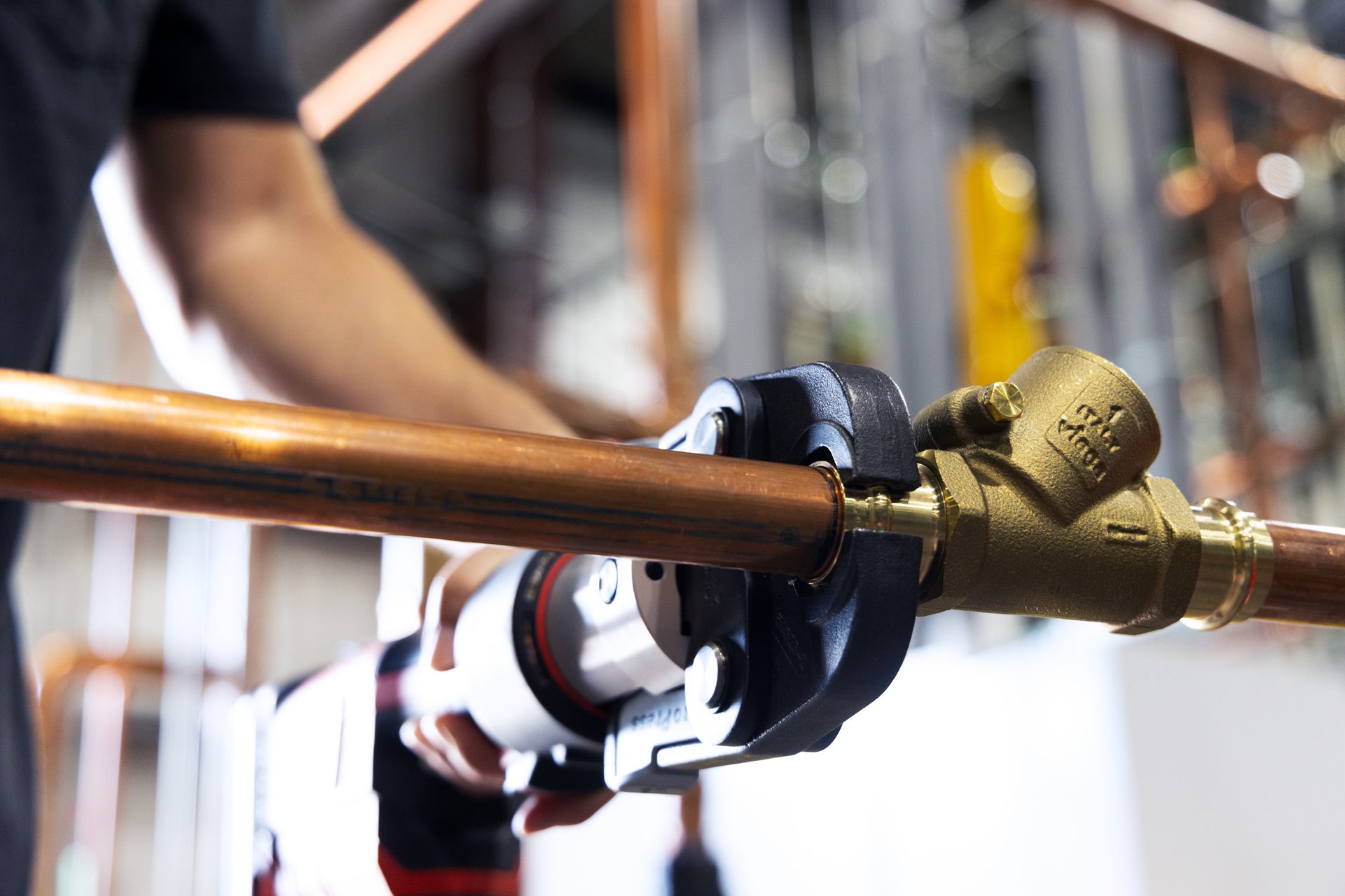 Person pressing copper pipe onto a brass fitting with a specialized tool.