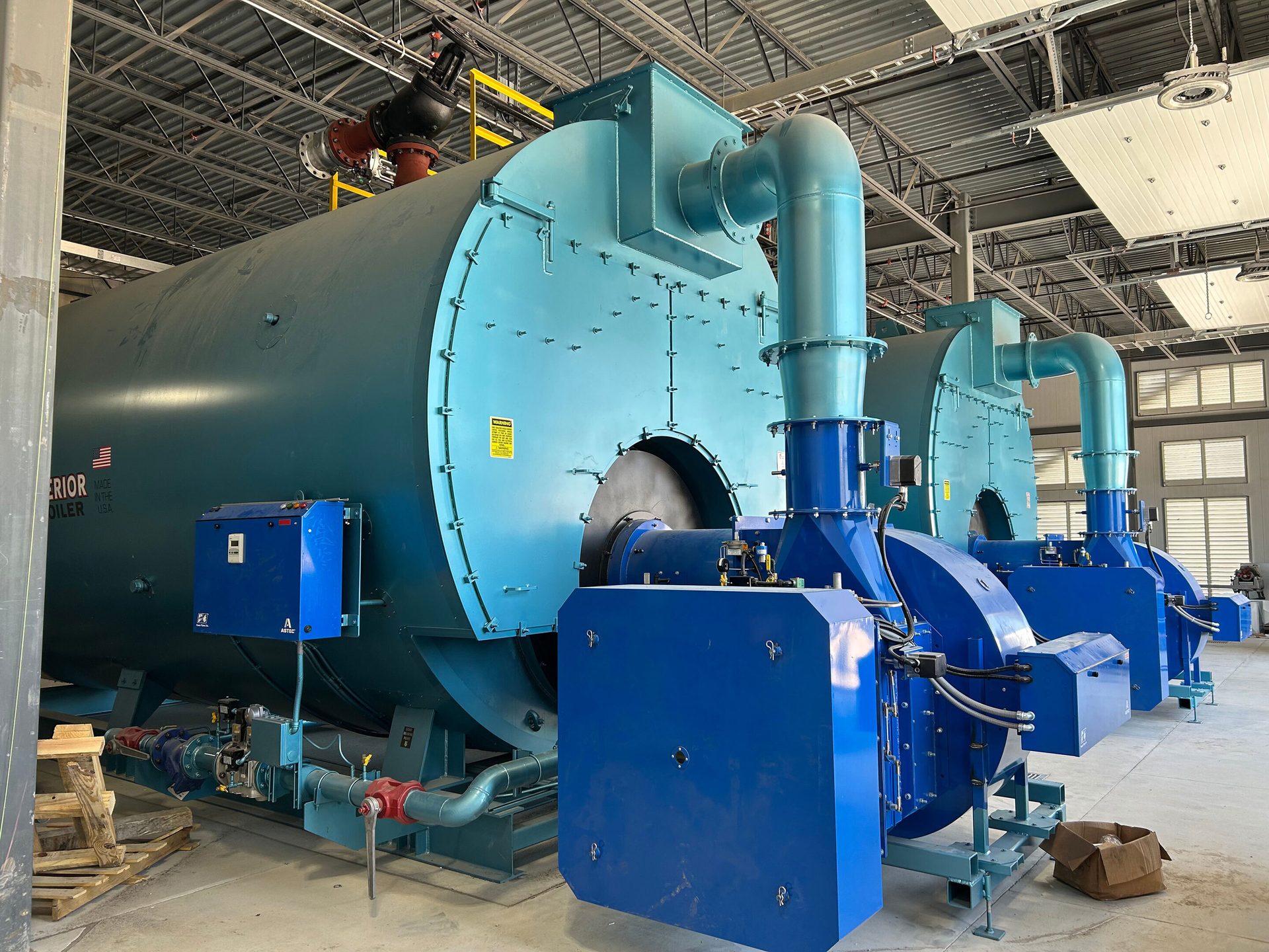 Two large blue industrial boilers in an unfinished building.