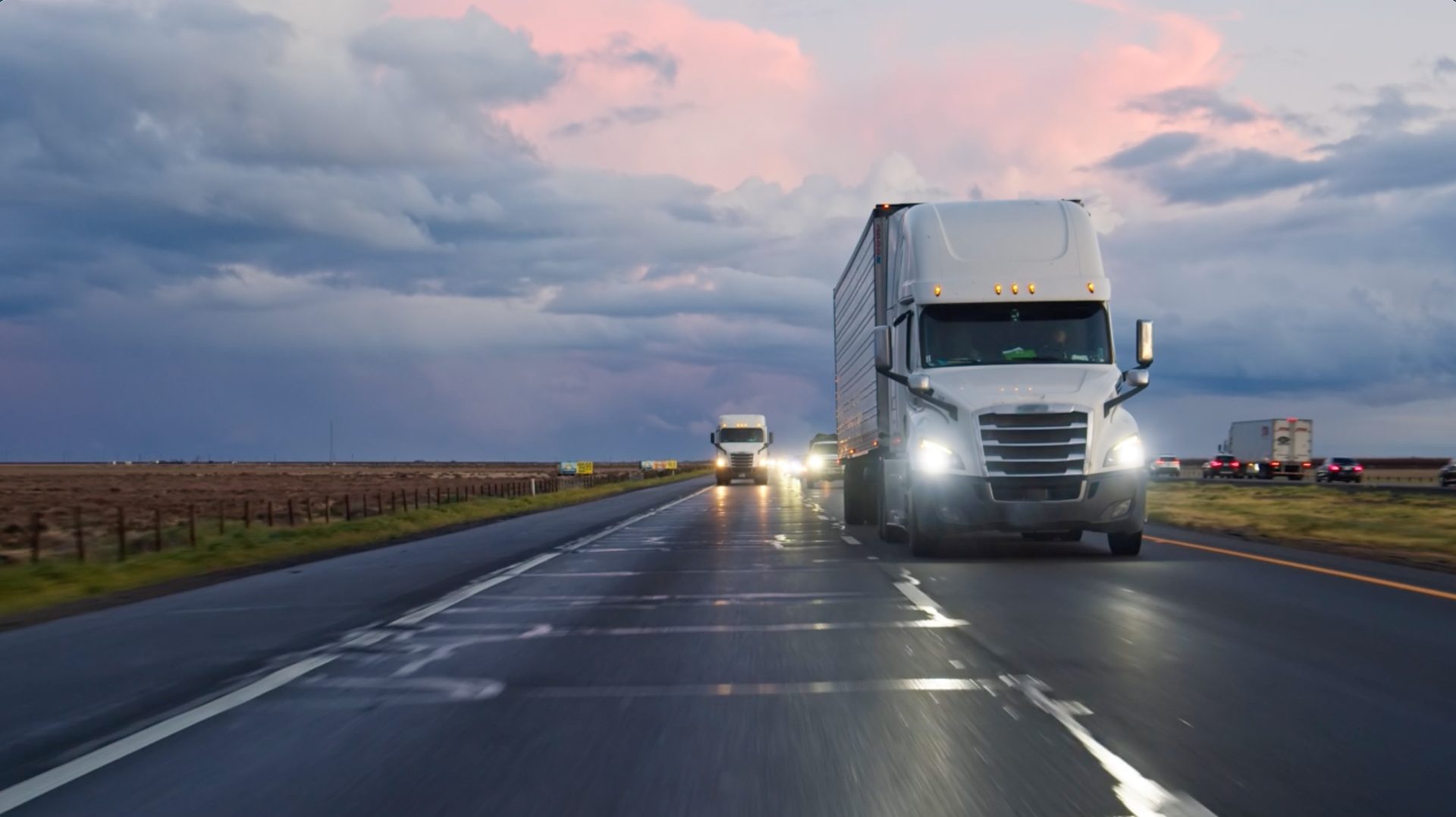 Trucks on a wet highway with dramatic clouds at dusk.