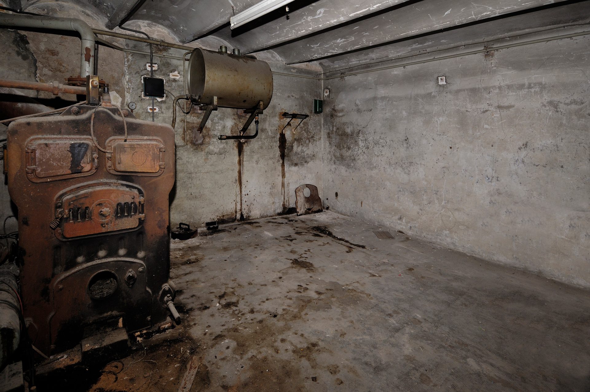 Dirty, old basement with a rusty boiler and a horizontal tank.
