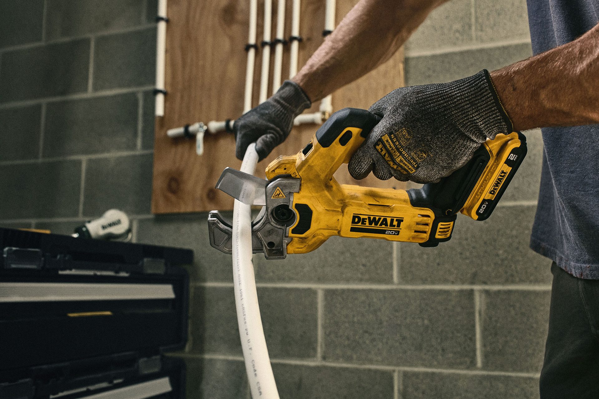 Person in gloves cutting a white pipe with a yellow DeWalt power pipe cutter.