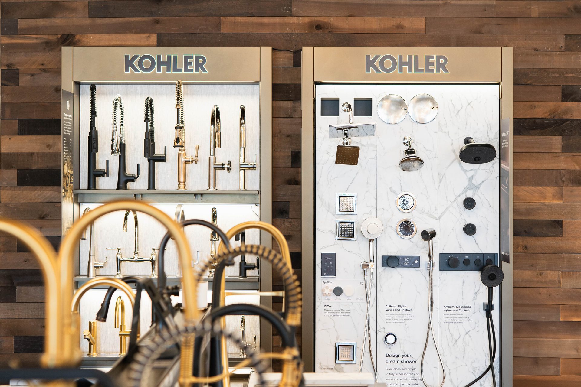 Kohler display stands with kitchen faucets and shower systems on a wooden wall.
