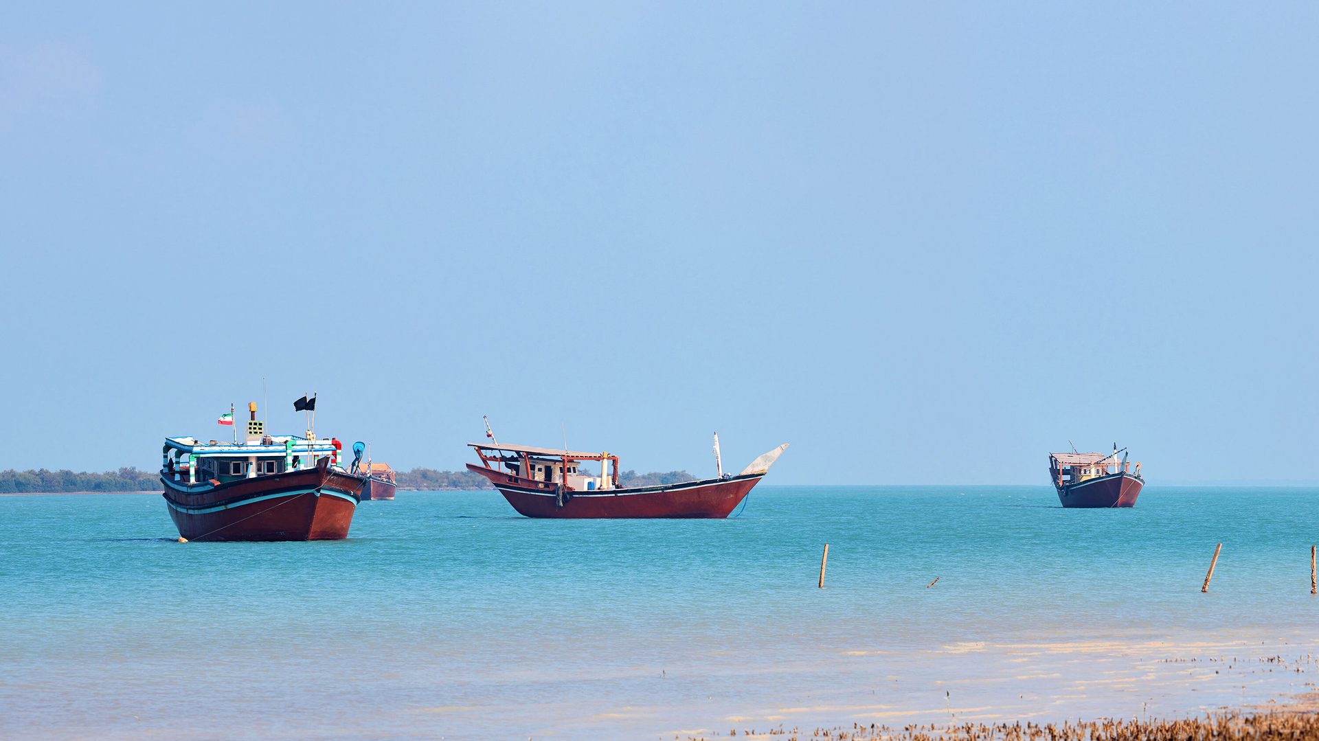 Three traditional boats on calm turquoise water under a clear sky.