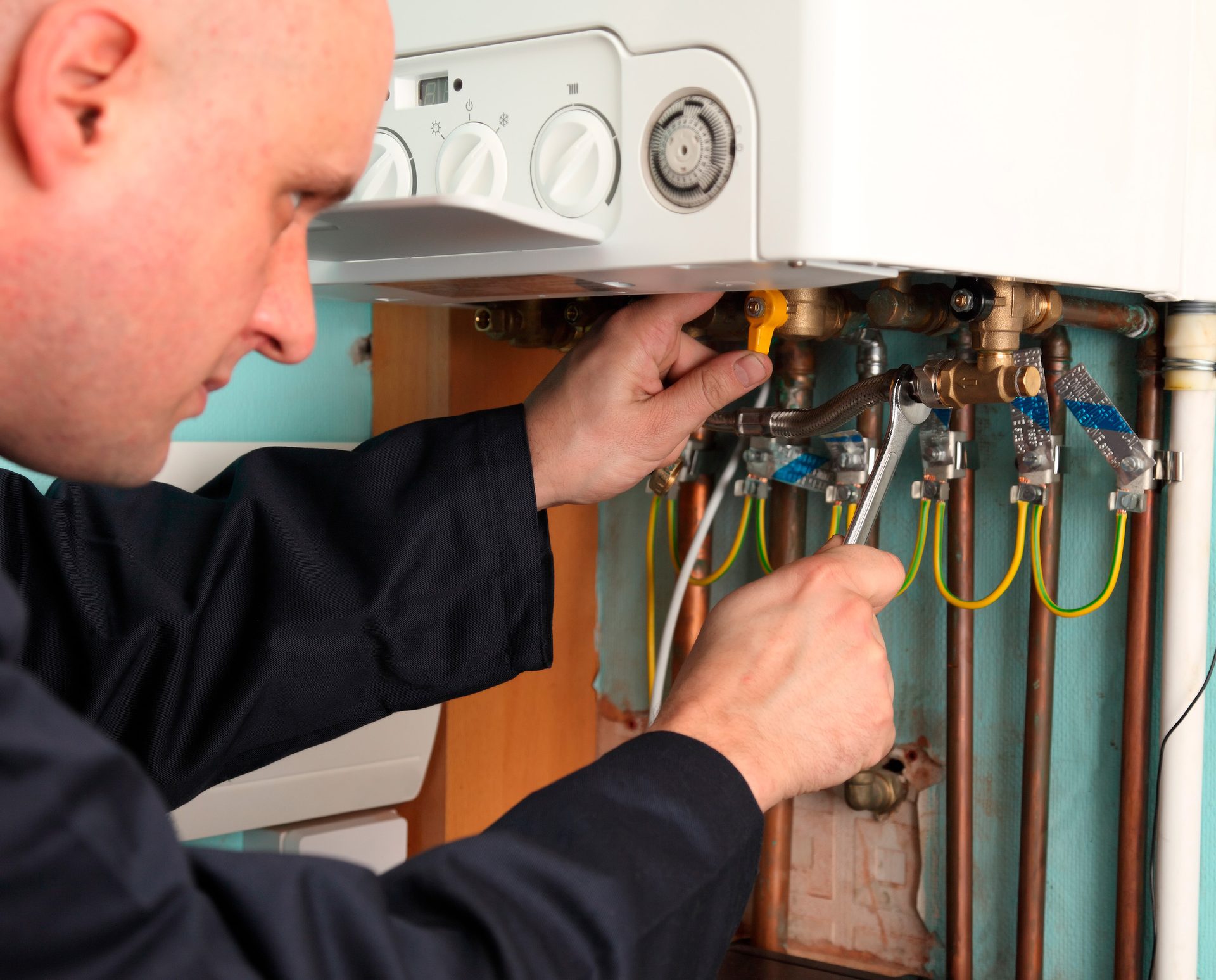 Plumber adjusting a boiler's pipes with a wrench and turning a valve.