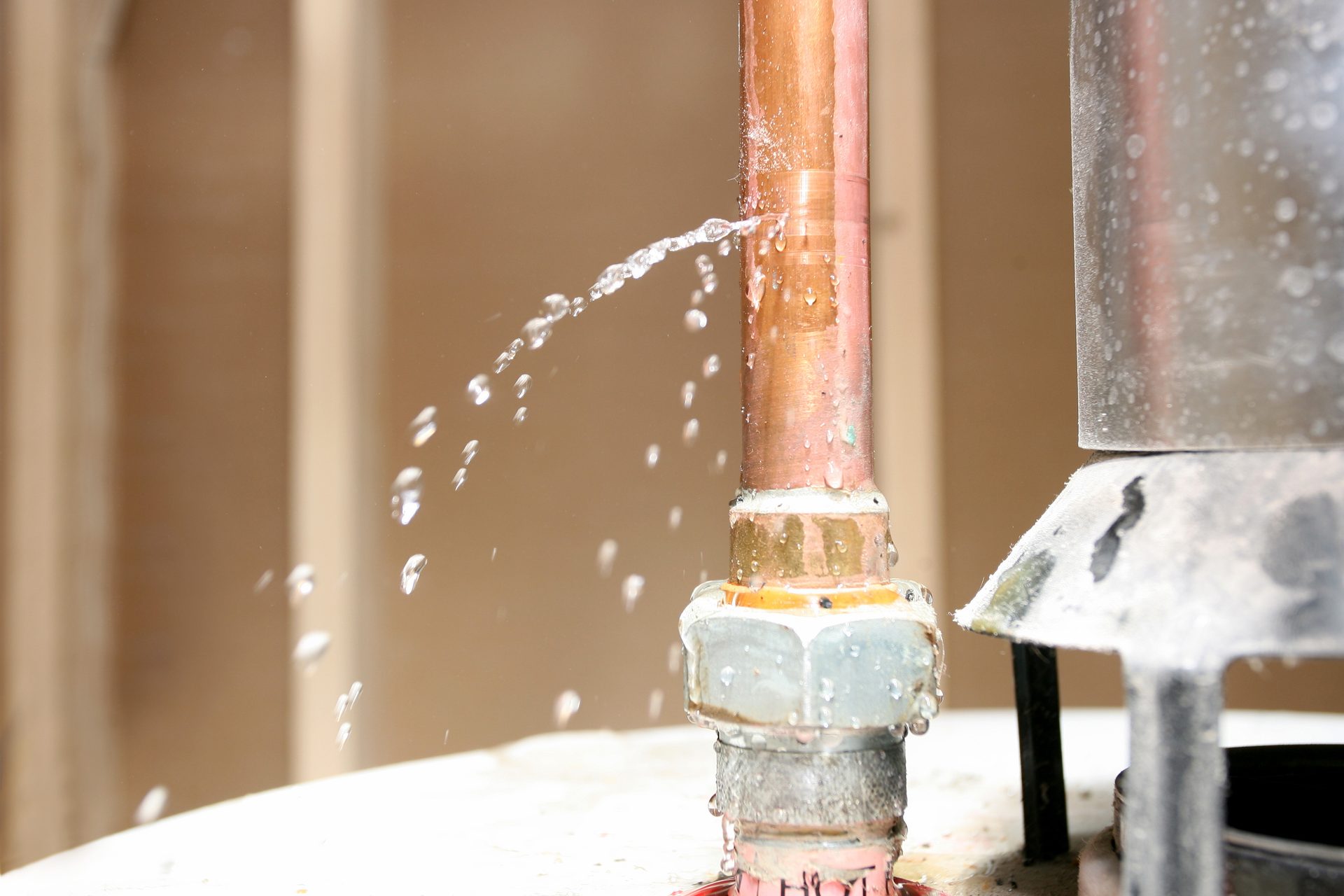 Leaking copper pipe with water spraying out, next to a water heater.