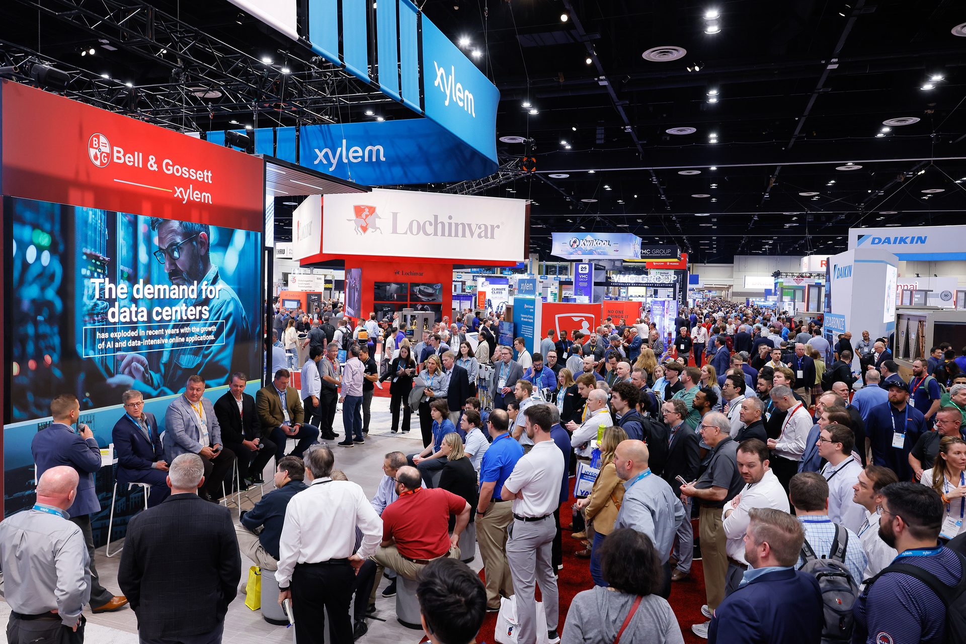 Crowded exhibition hall with Bell & Gossett, Xylem, Lochinvar, and Daikin booths.