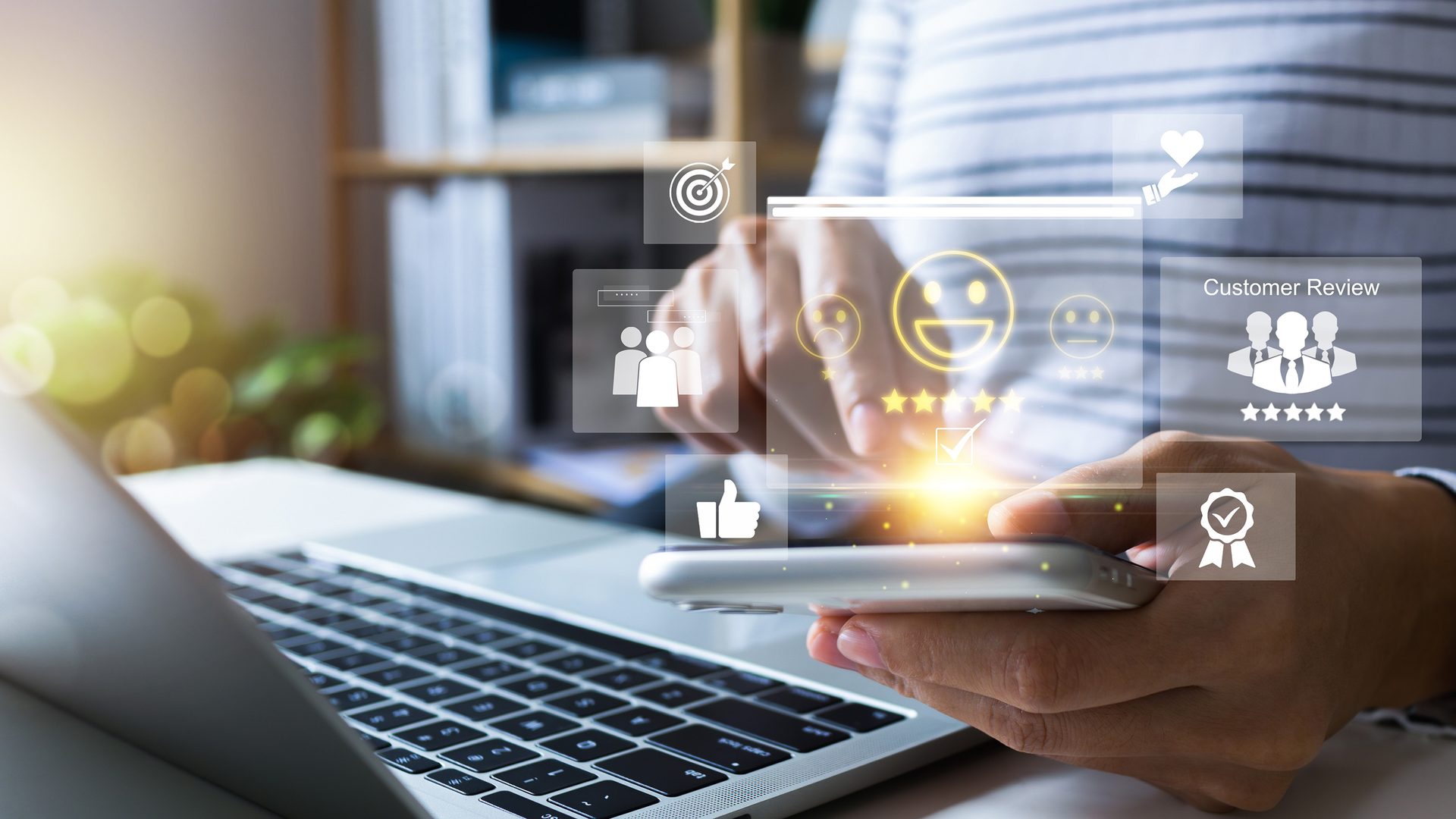 Person using a smartphone with glowing customer review and satisfaction icons; laptop in foreground.
