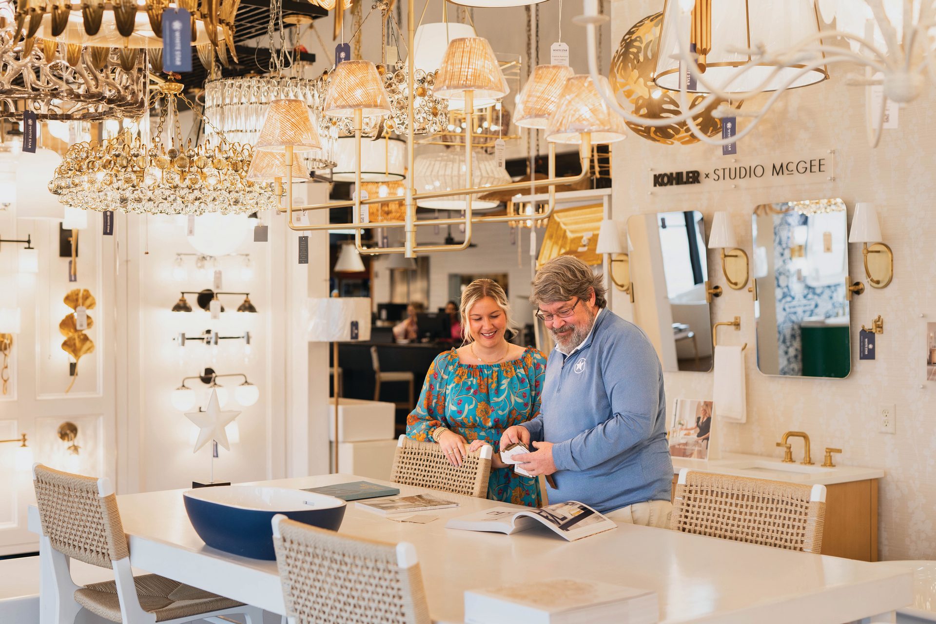 Two customers review items at a table in a lighting and home decor showroom.