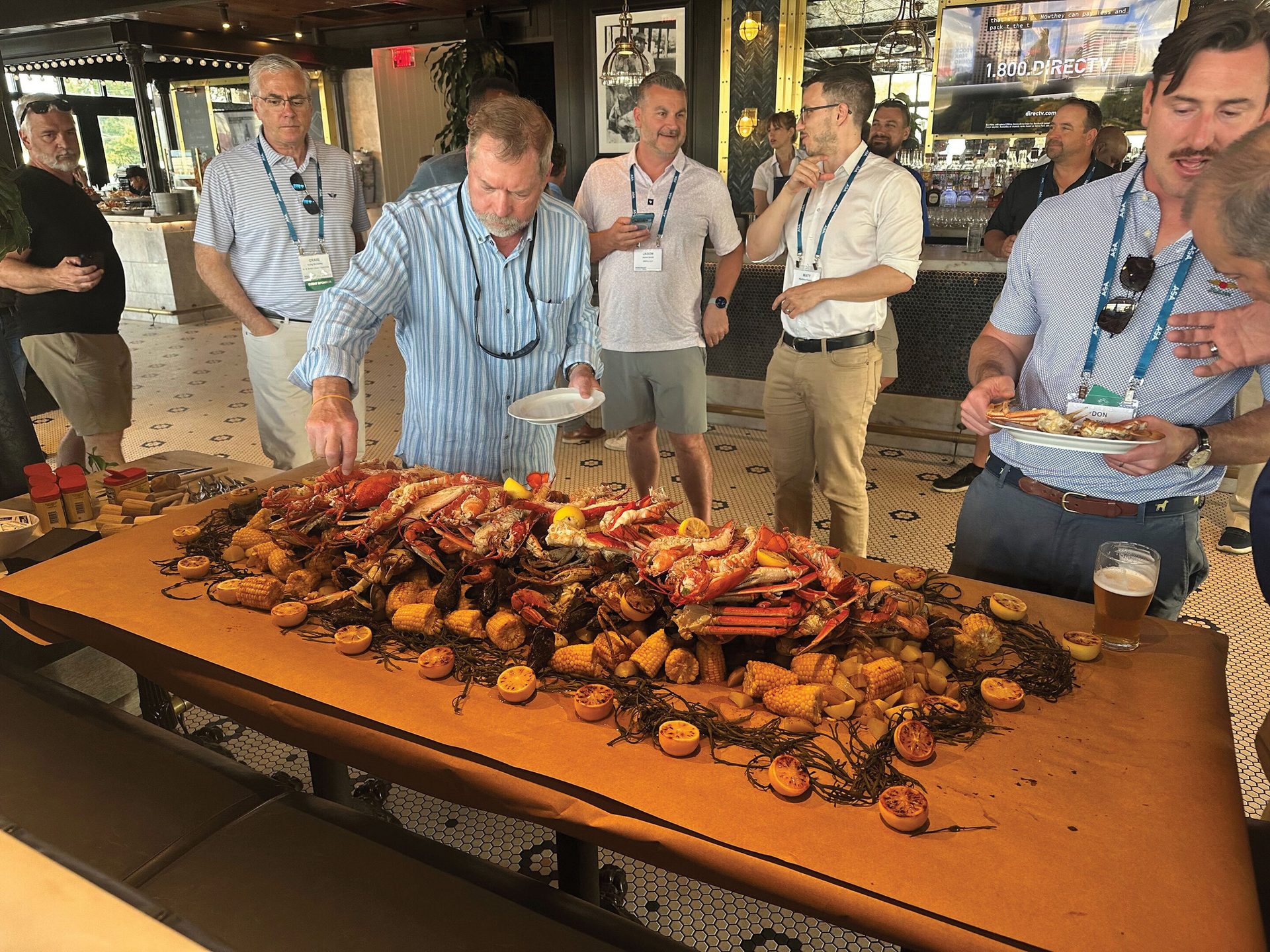 A group of men gathers around a long table laden with a large seafood boil.