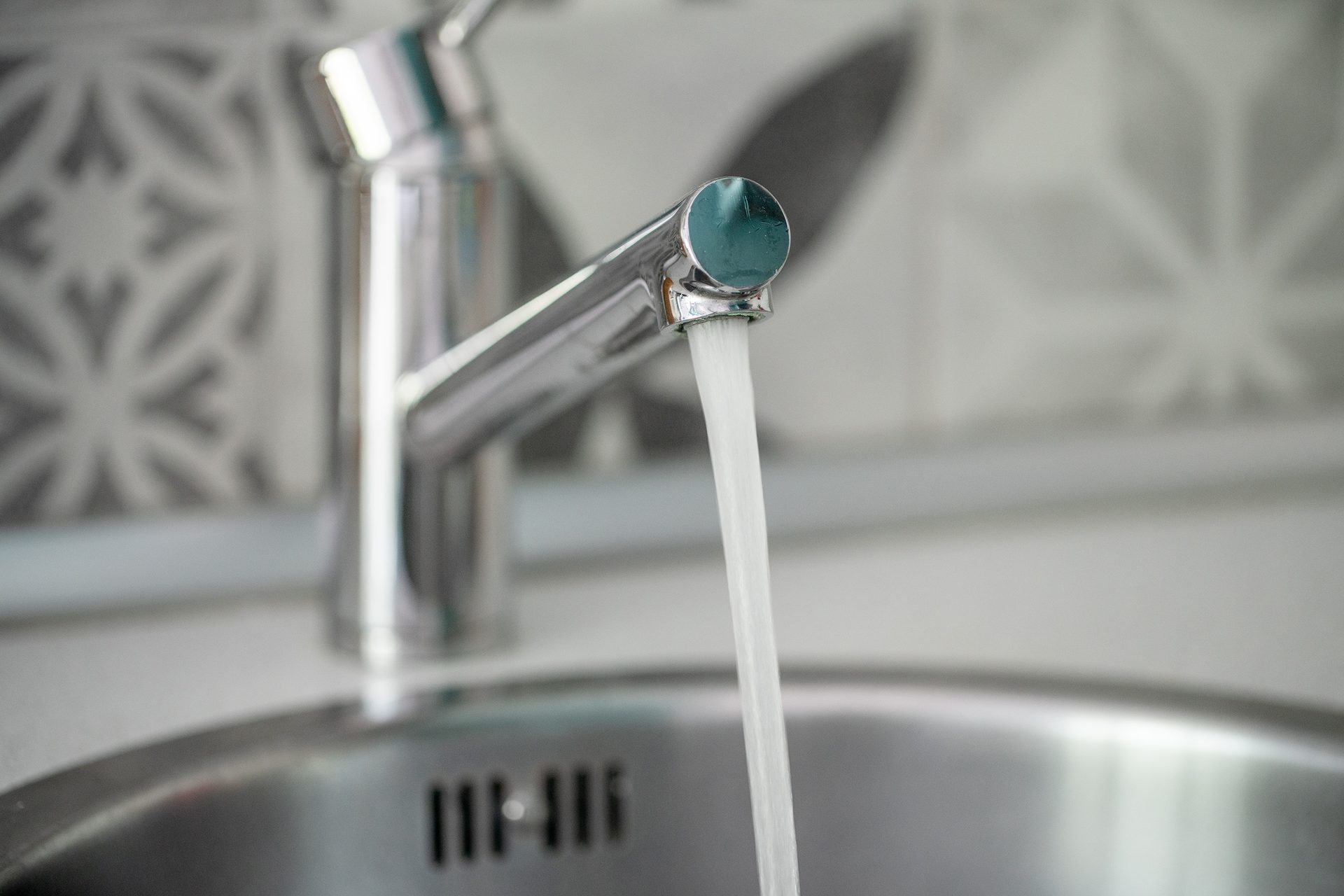 Water streams from a chrome kitchen faucet into a metal sink.