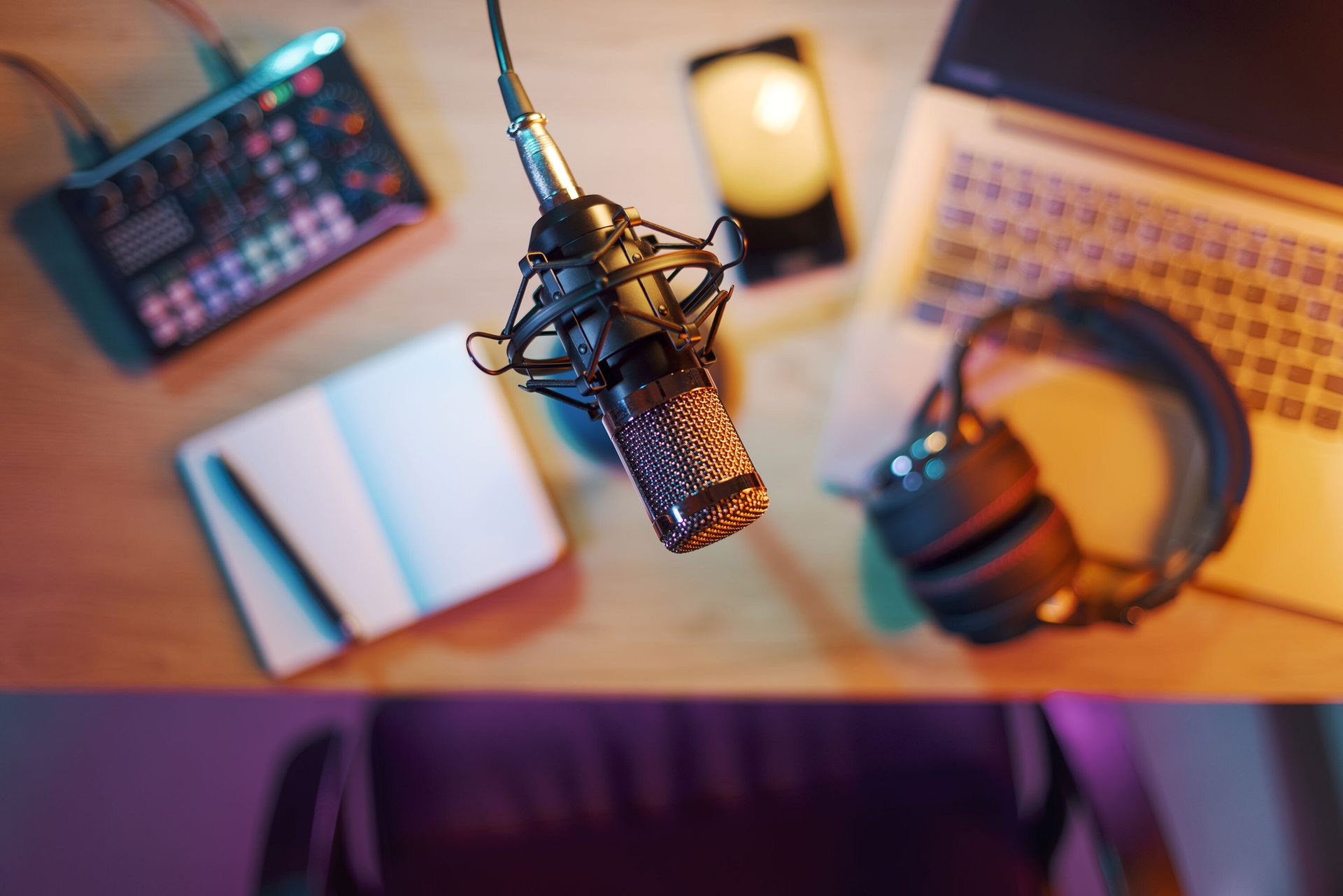 Overhead view of a podcasting desk with a microphone, headphones, laptop, and sound mixer.