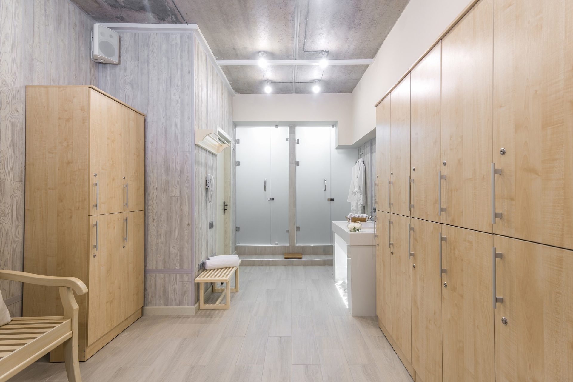 Locker room with light wood lockers, frosted glass showers, and a concrete ceiling.