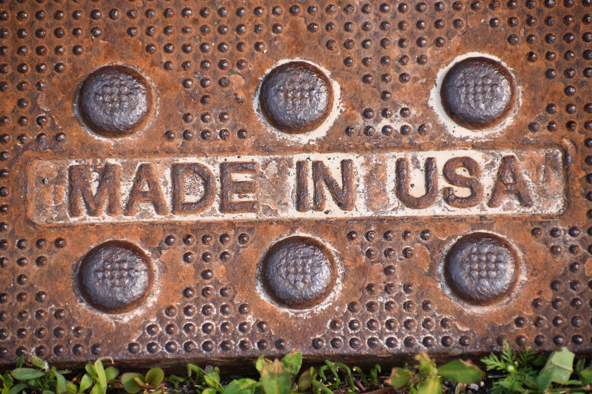 Rusty metal plate embossed with "MADE IN USA," surrounded by raised circles and dots.