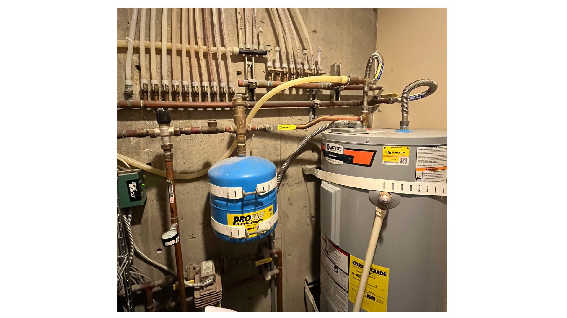 Water heater, blue expansion tank, and copper/PEX plumbing manifold on a concrete wall.